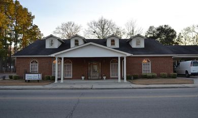 Brick civic building with white columns, dark roof, and parked van at the entrance