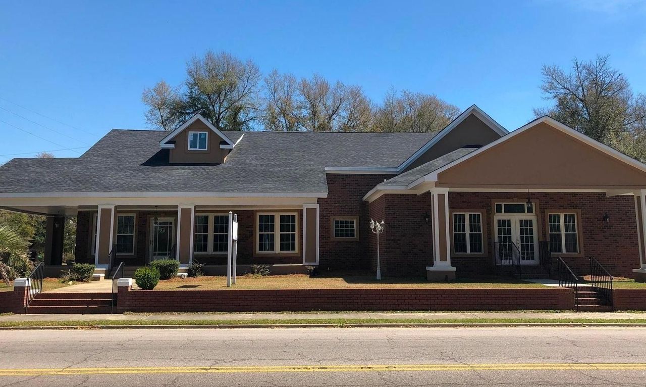 Single-story brick building with a covered porch and dormer windows beside a road