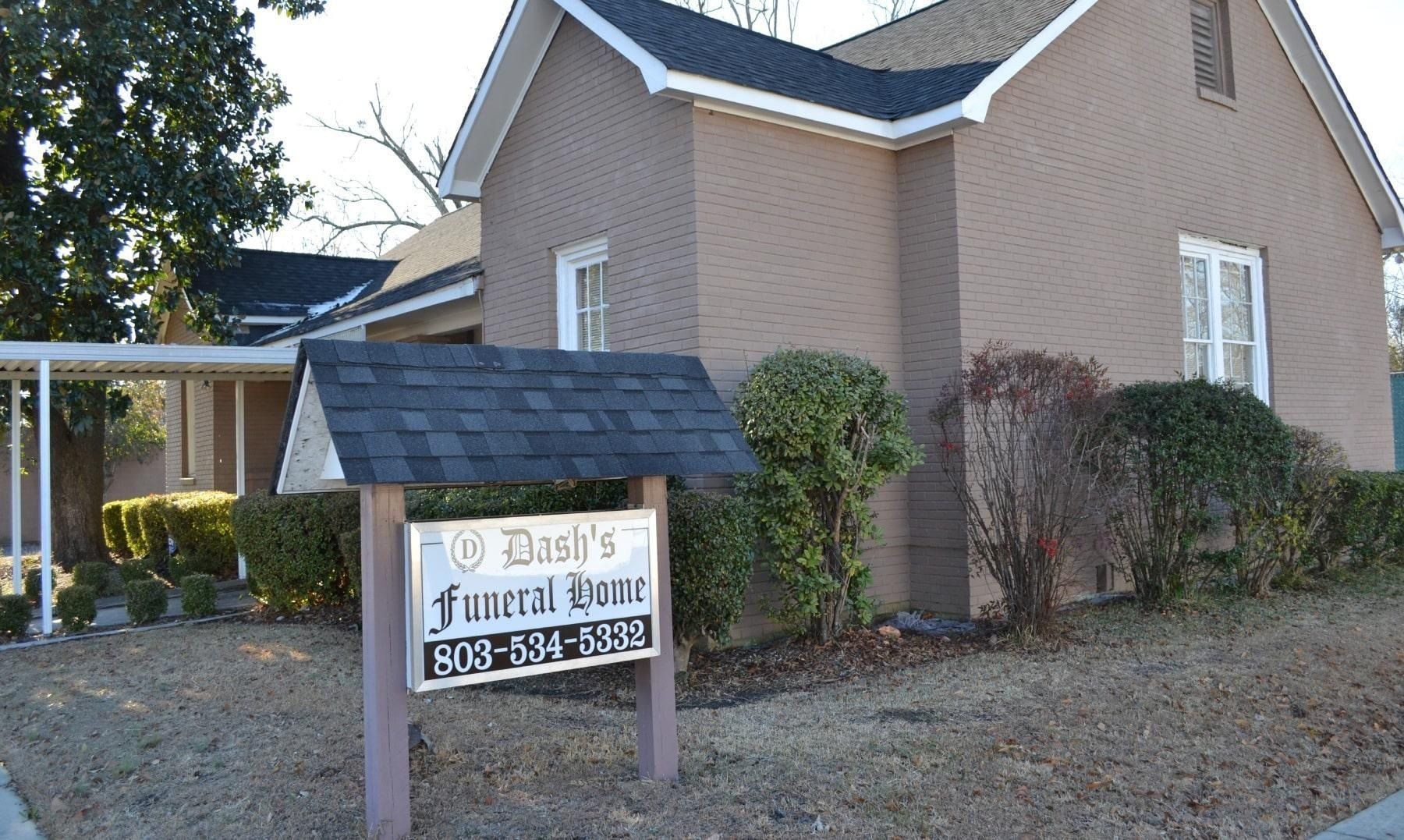 Brick church building with white trim and a sign in front near a covered walkway.