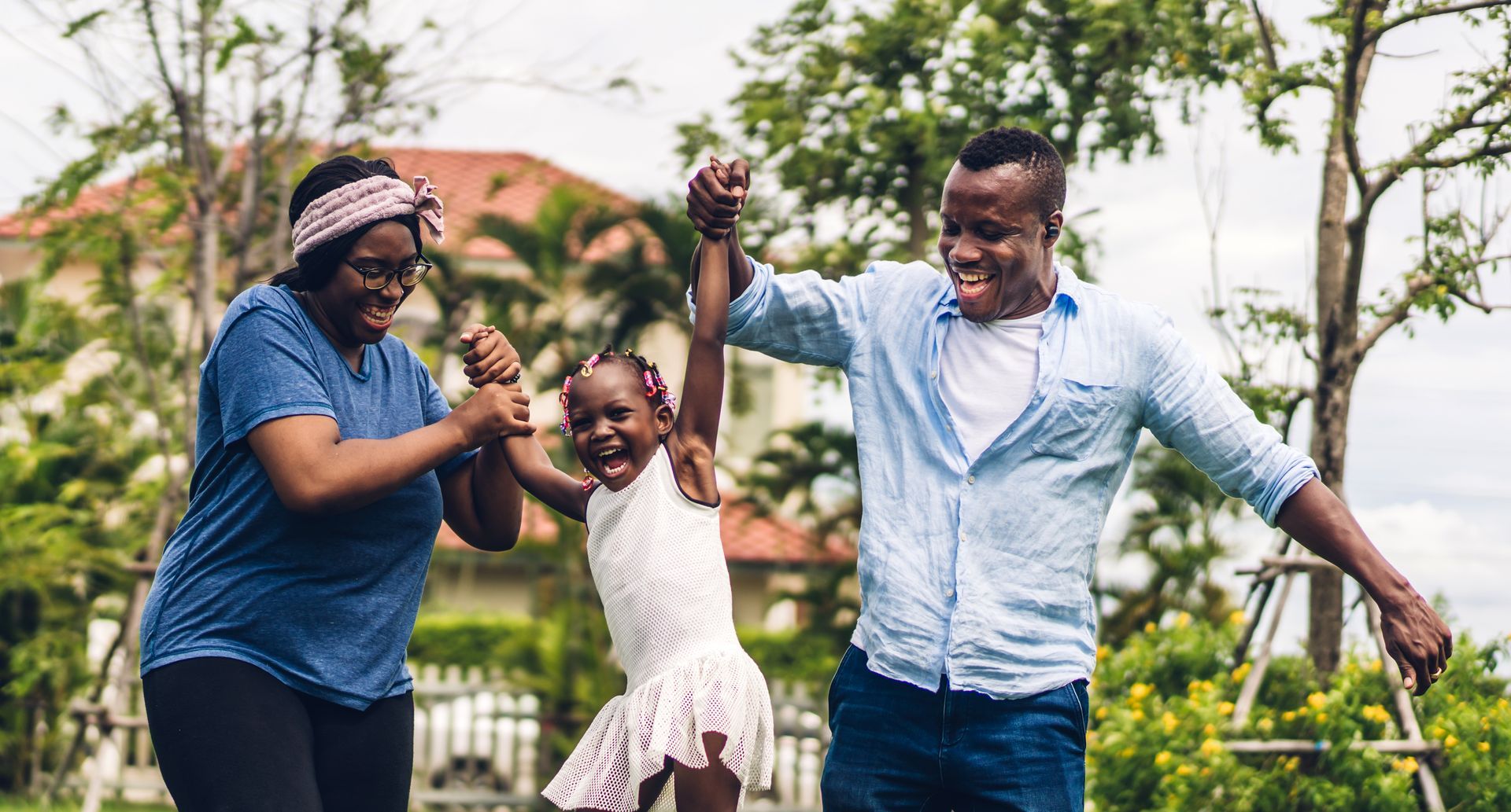 Three people smiling and holding hands while dancing outdoors in a sunny park