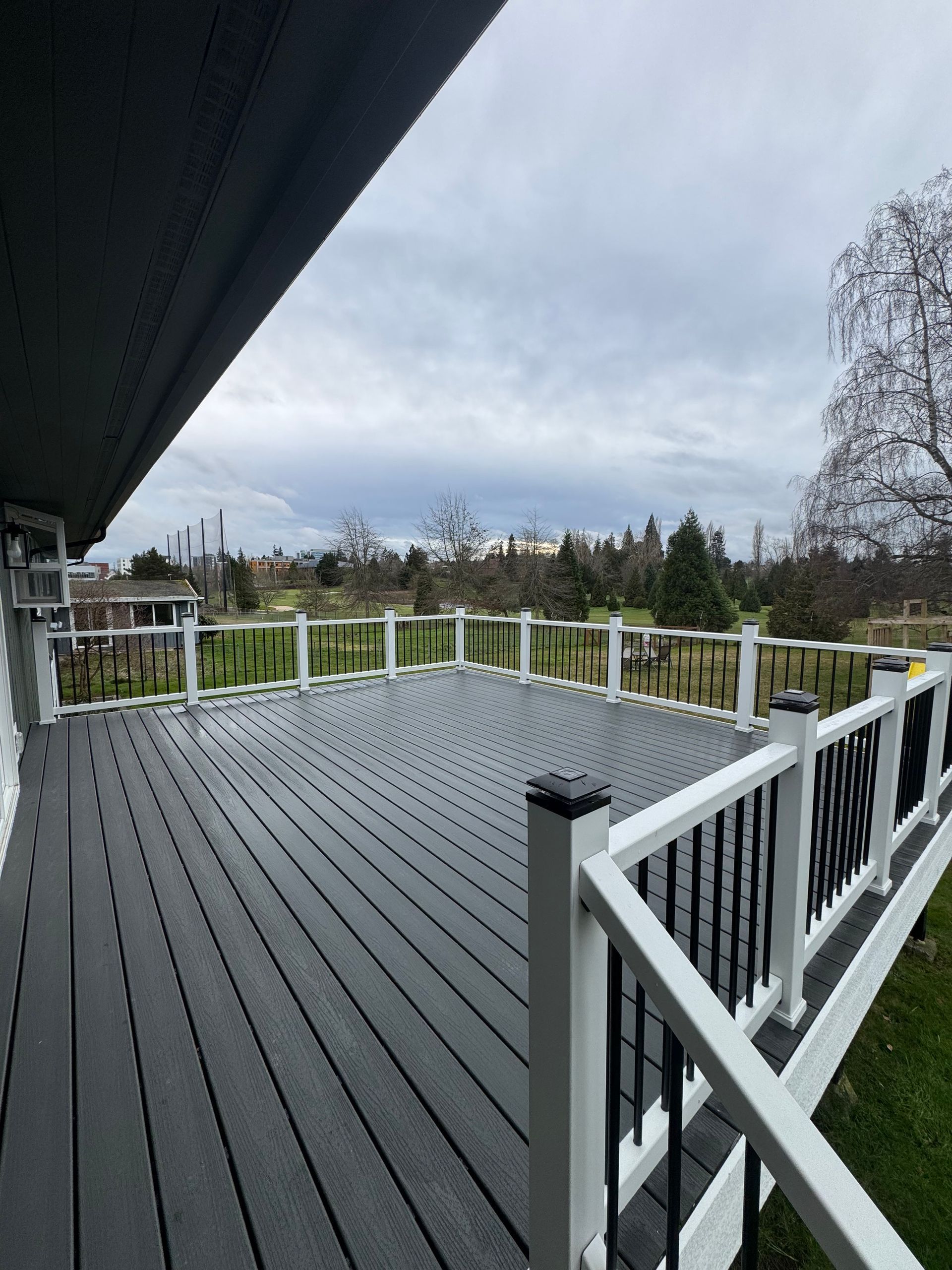 Spacious gray deck with white railings overlooking a cloudy backyard and trees