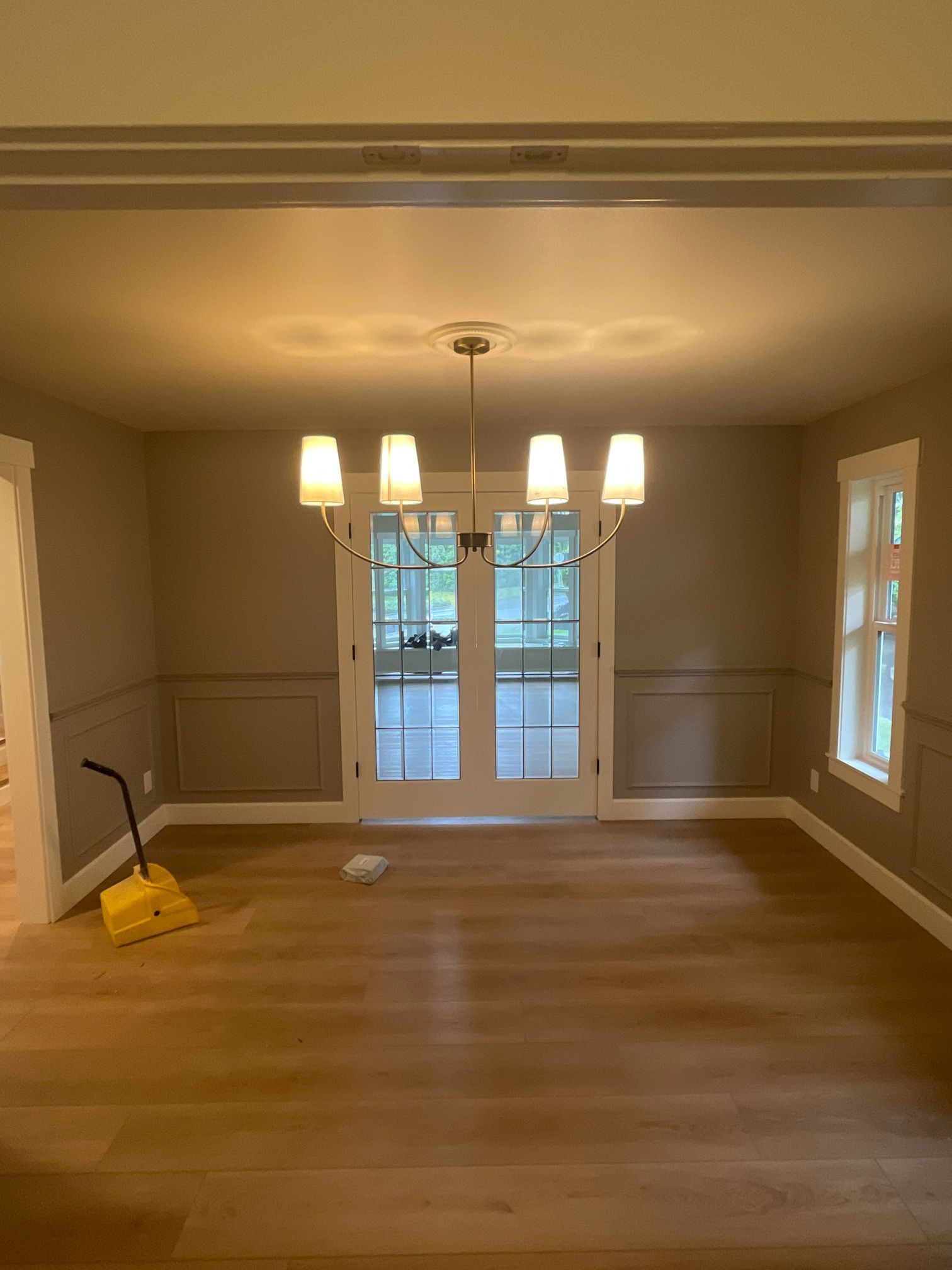 Empty dining room with hardwood floors, chandelier, and a yellow broom and dustpan near the left wall.