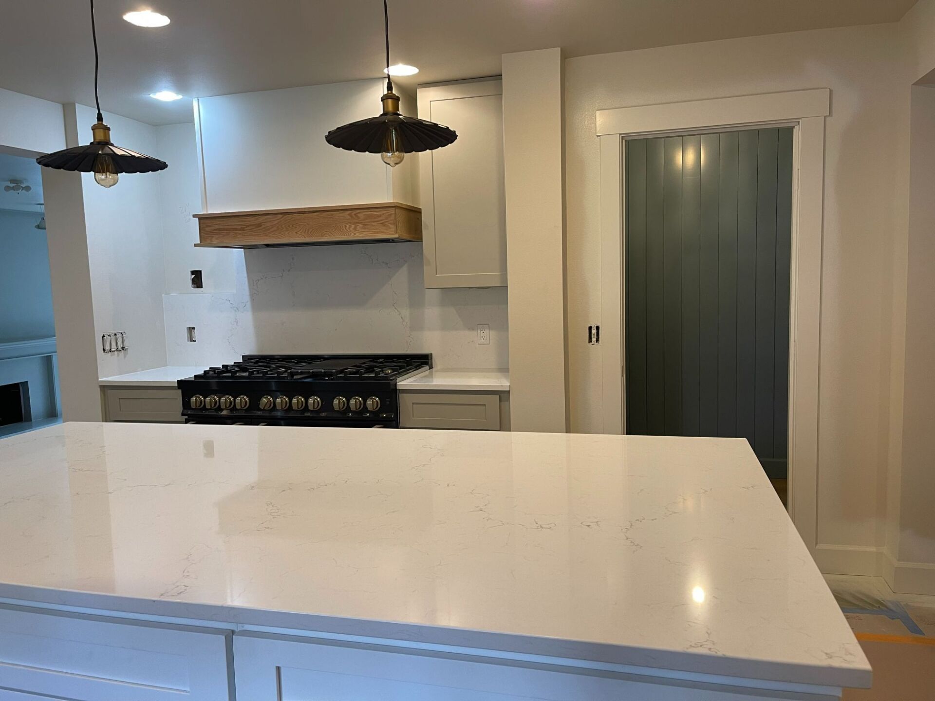 Modern kitchen with white island, black stove, pendant lights, and glass pantry door
