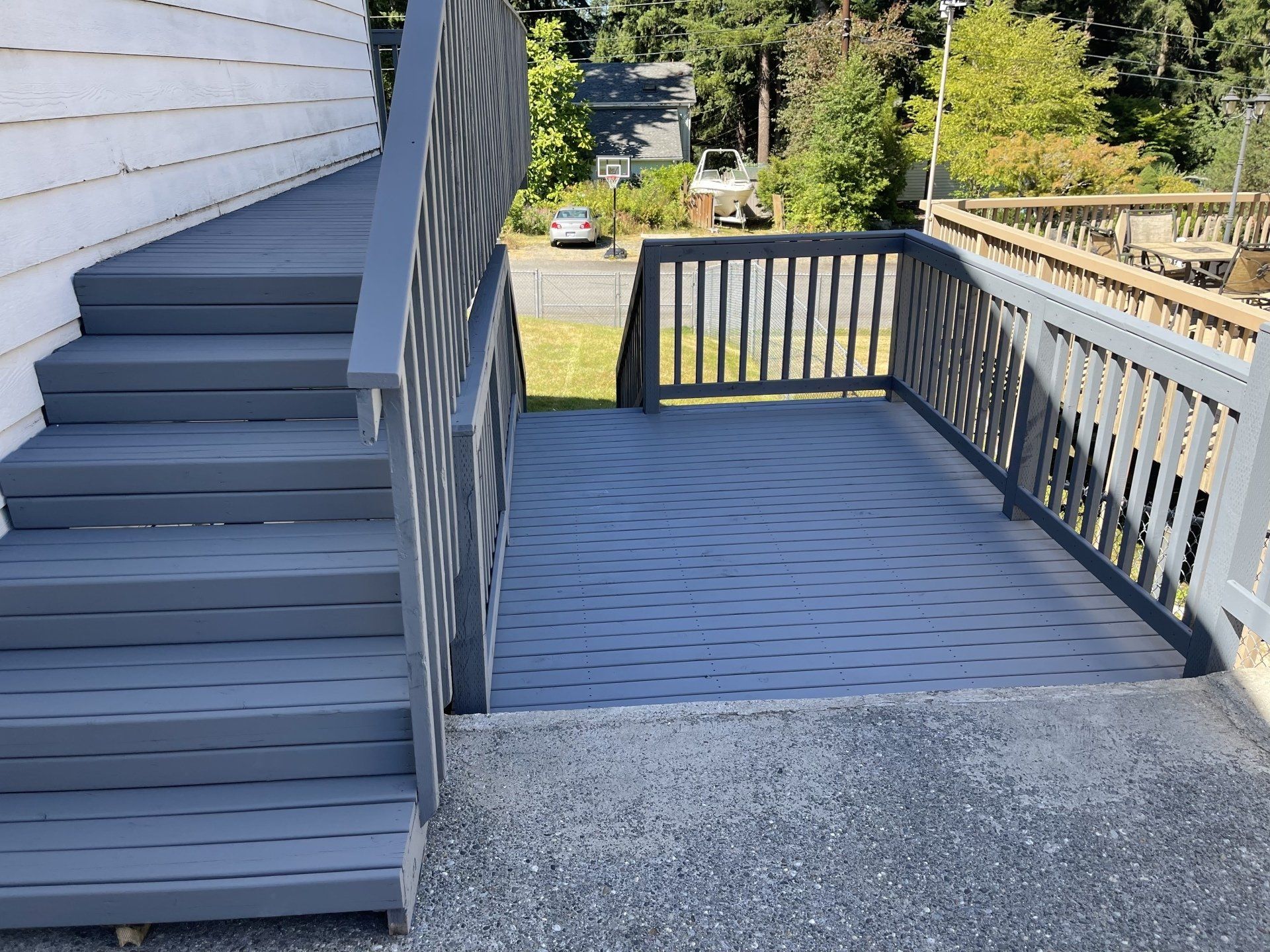 Gray deck and stairs adjacent to a white house, with a gravel patio.