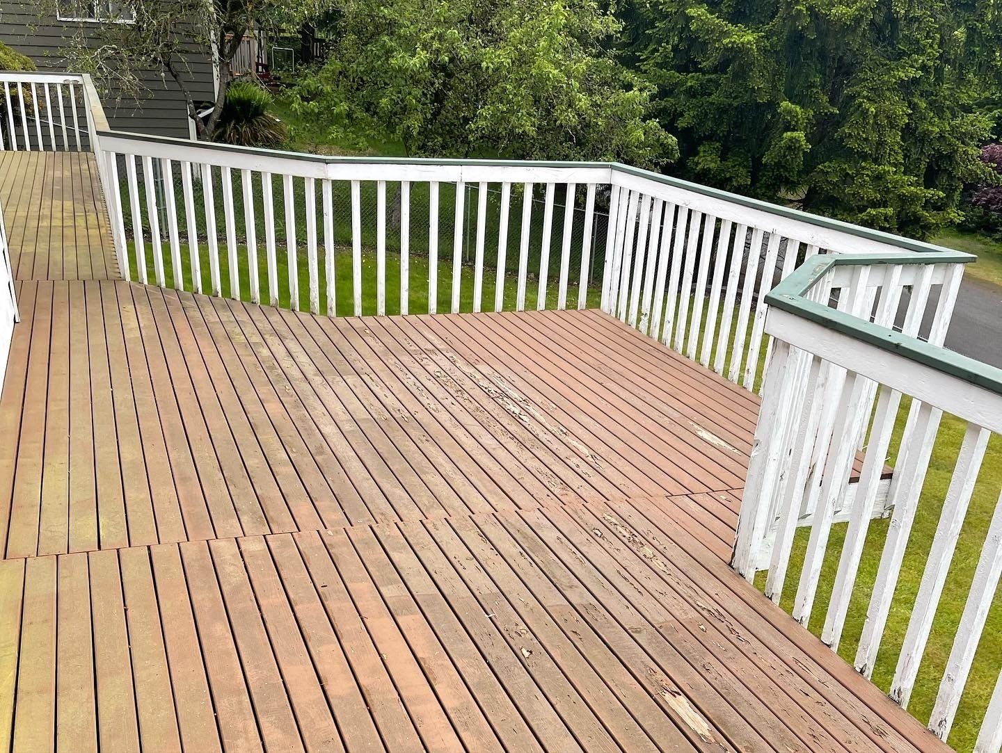 Wooden deck with white railings, looking worn. Grass and trees in the background.