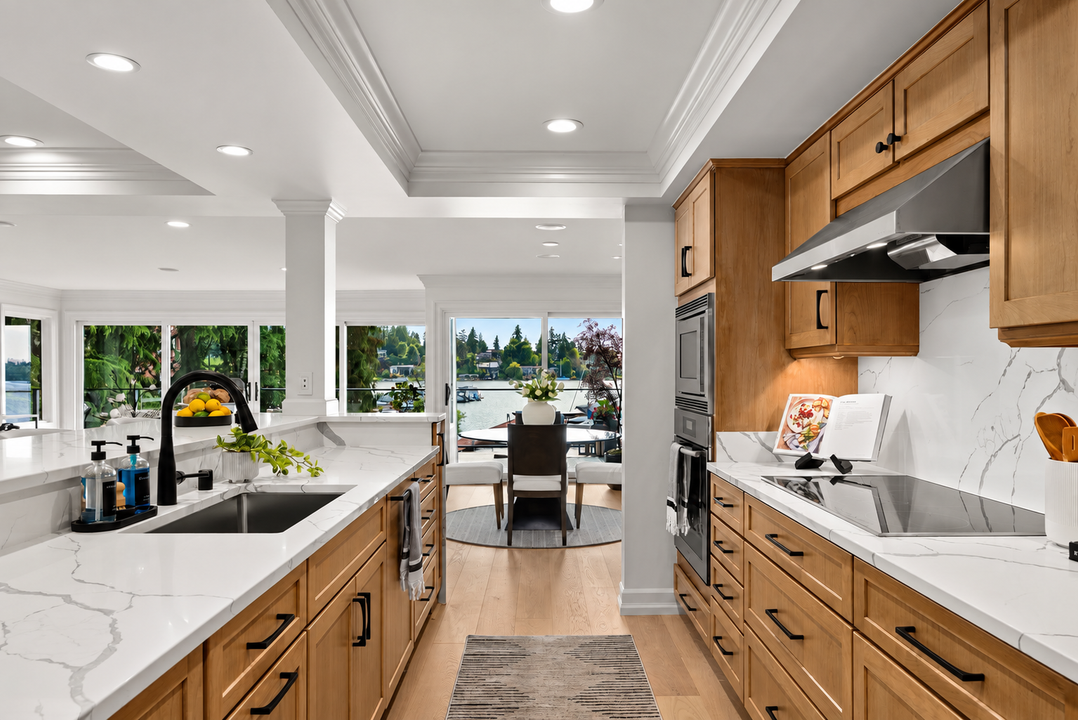 Bright modern kitchen with white counters, wood cabinets, and an island opening to a dining area and backyard.