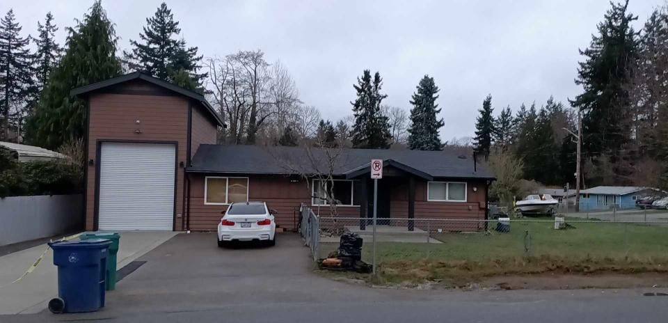 Brick house with attached garage, car in driveway, grass lawn, trees, overcast sky.
