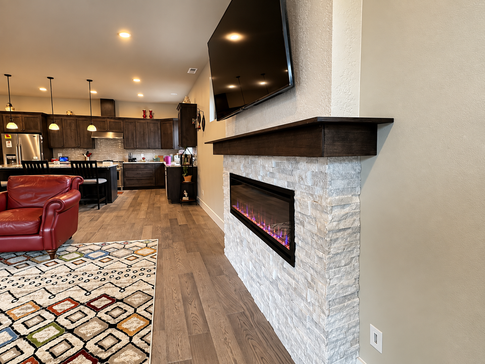 Modern living room with stone fireplace, wall-mounted TV, red sofa, and open kitchen beyond