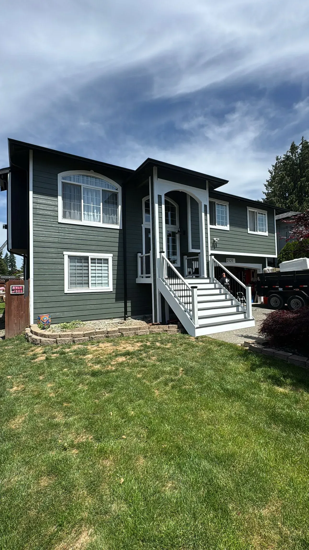 Two-story gray house with white trim, front stairs, and a green lawn under a cloudy sky