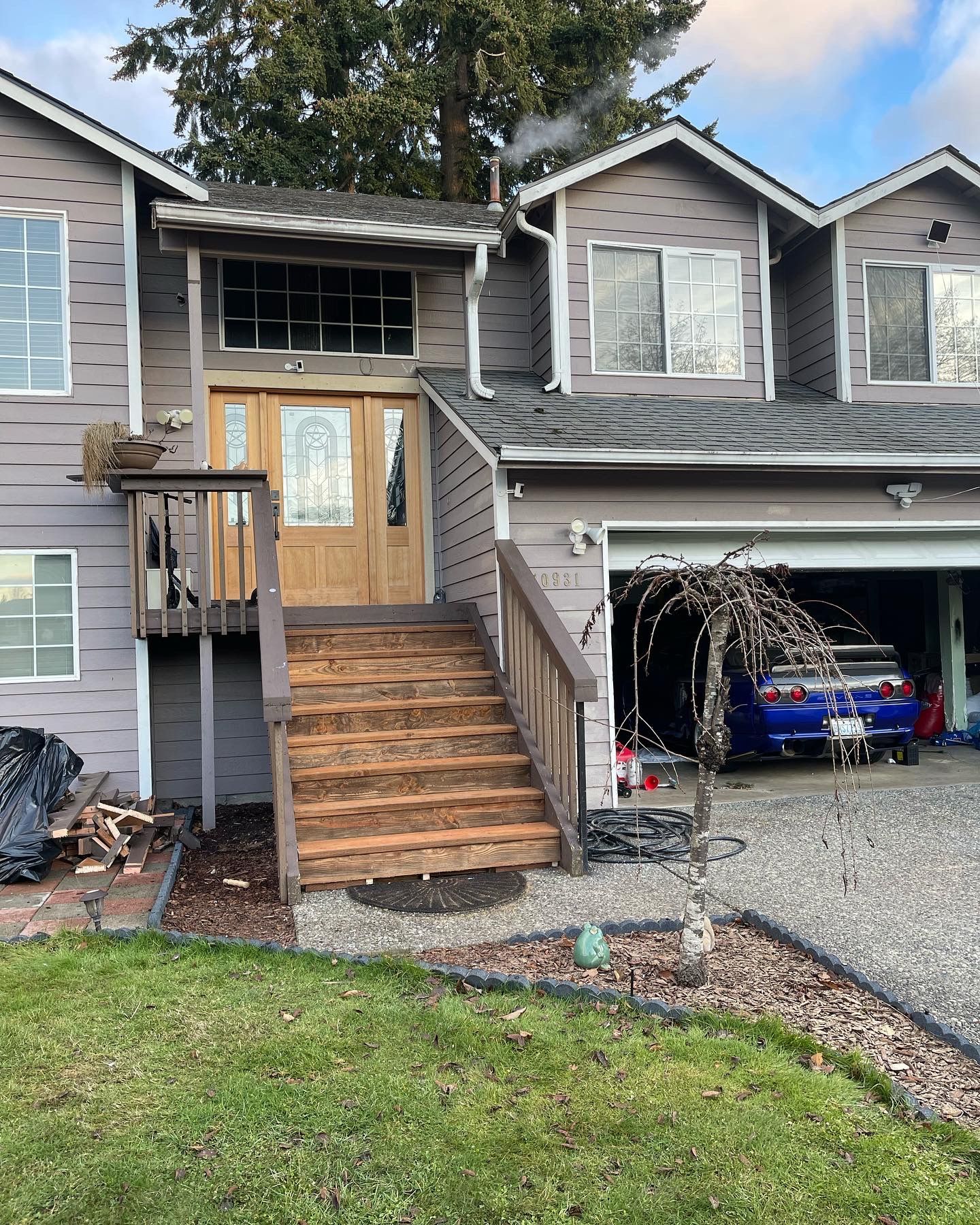 Two-story gray house with wooden steps, porch, and a car in the open garage.