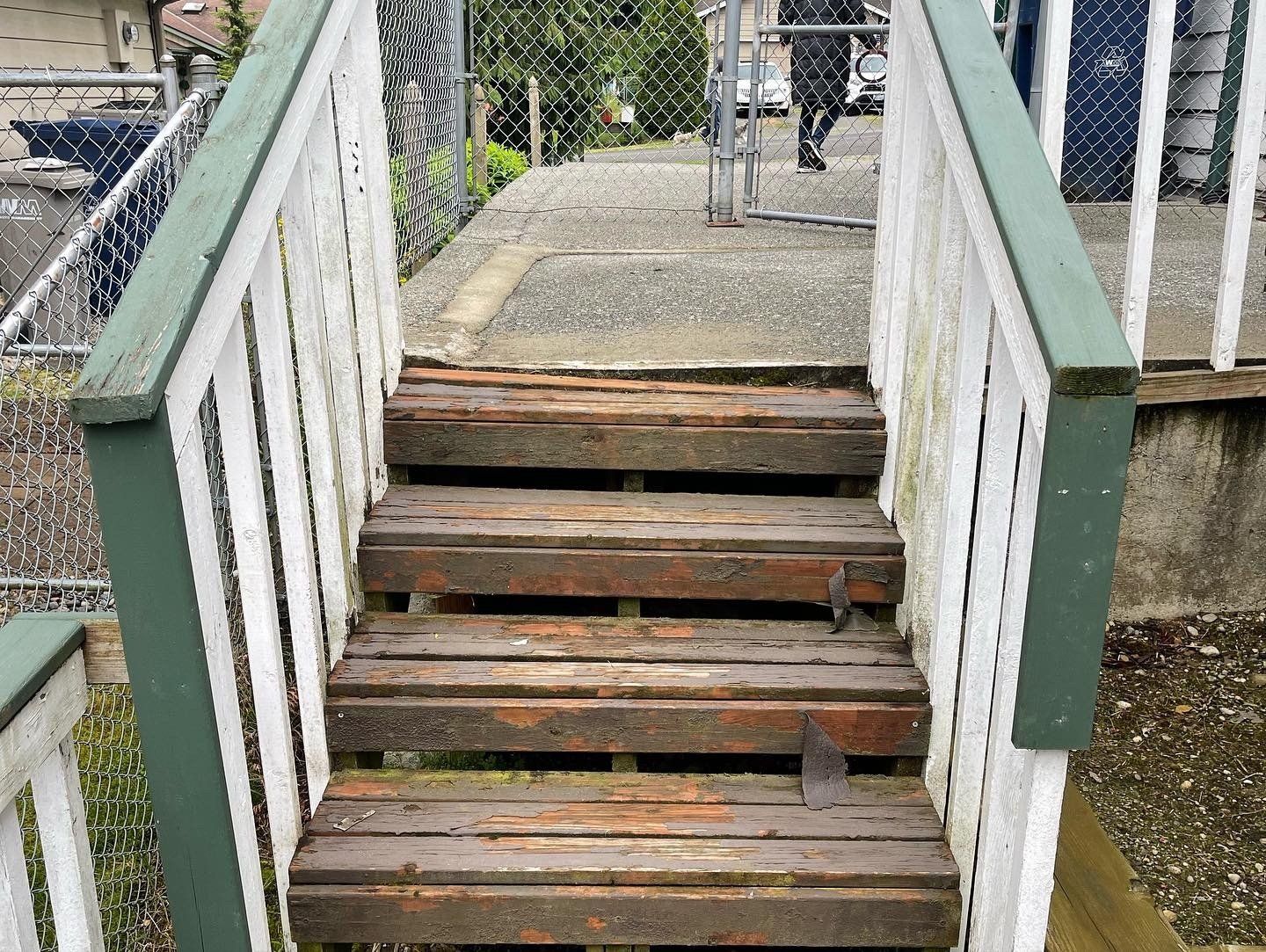 Wooden outdoor staircase with worn steps, white railings, and green trim.