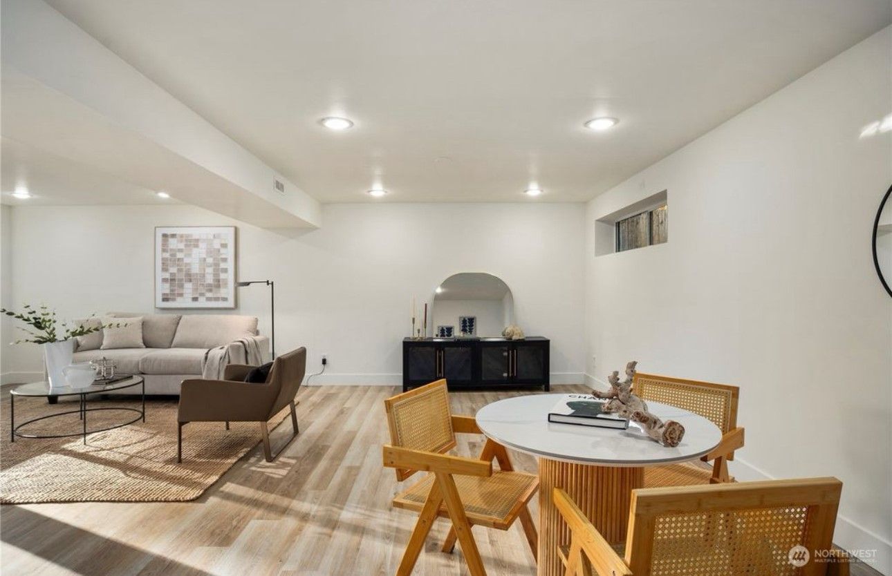 A bright, modern basement living space with seating areas, a dining table, and light wood floors.