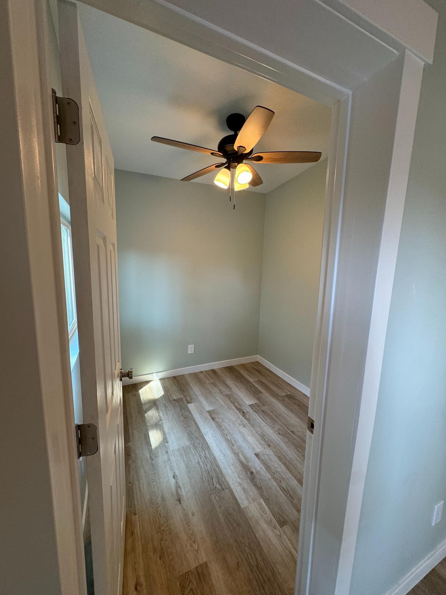 Open door leads to a small room with light wood floors, pale green walls, and a ceiling fan.