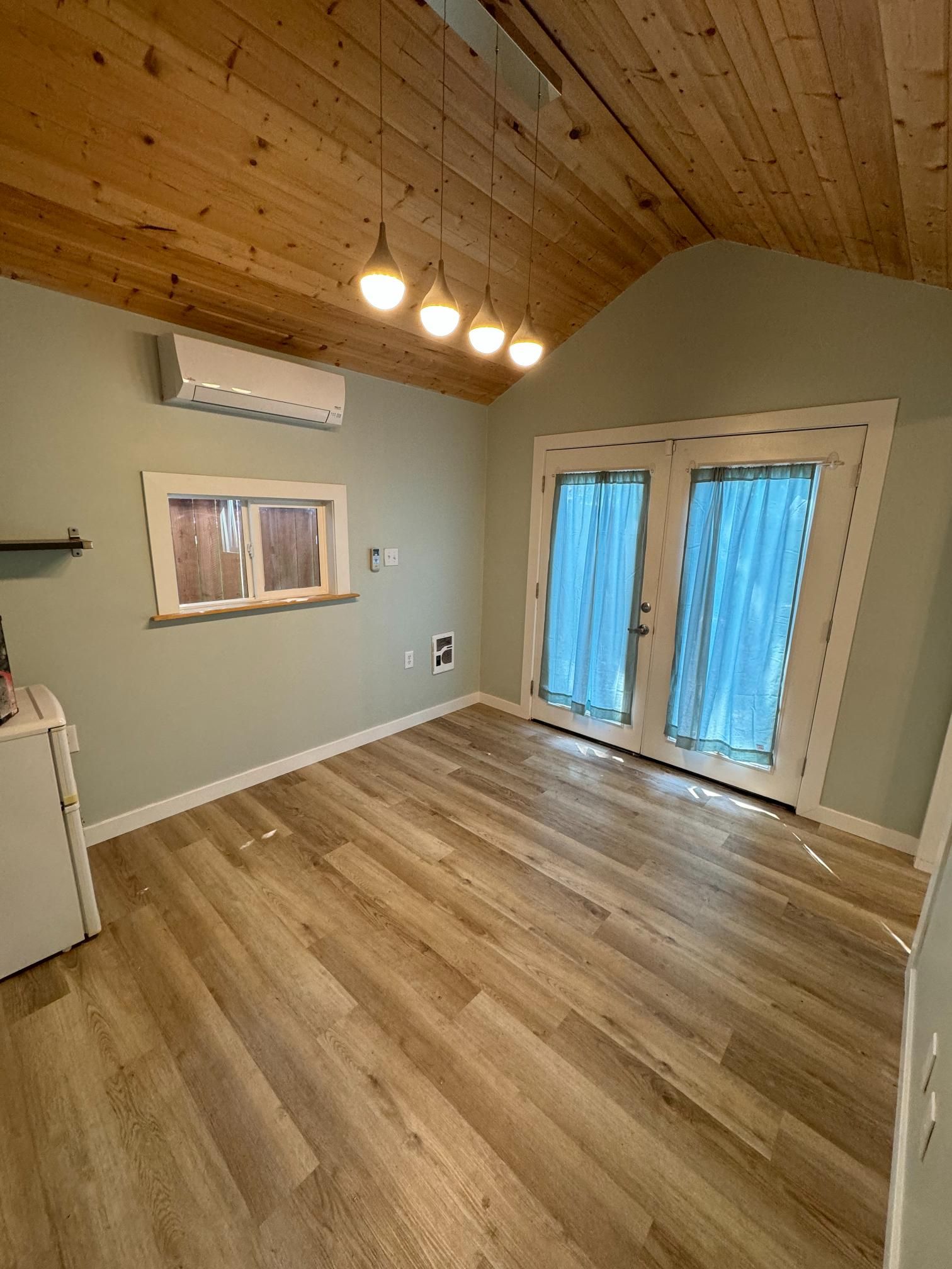 Interior room with light wood floor, green walls, French doors, wood ceiling, and pendant lights.