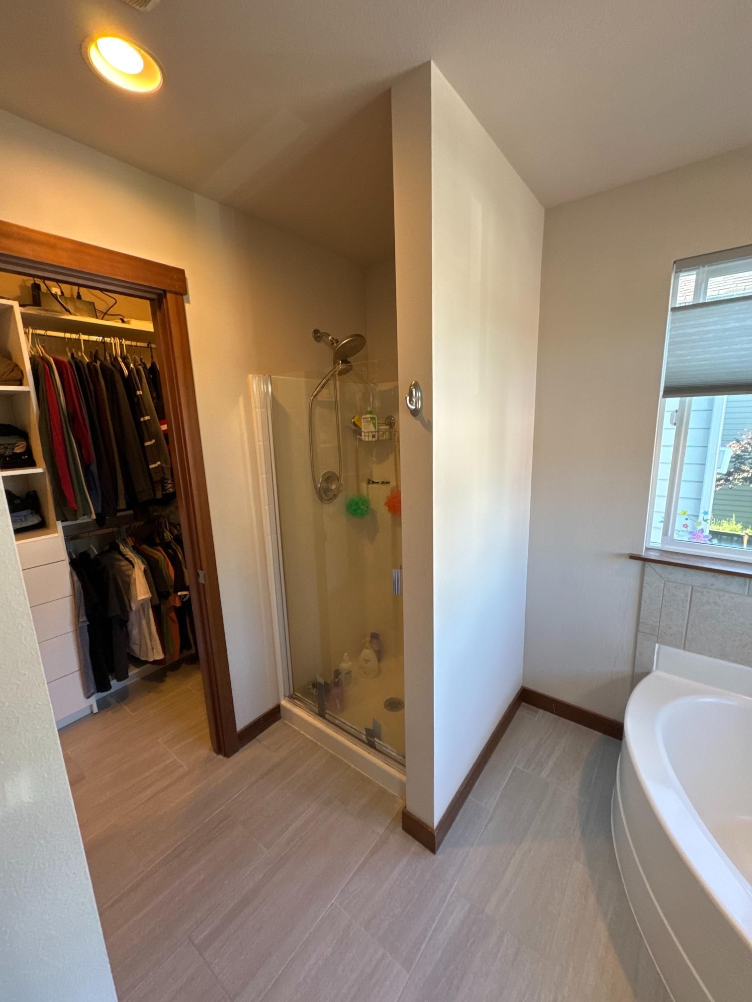 Bathroom with a walk-in closet, shower, and a curved bathtub. Beige walls, wood trim, and light gray flooring.