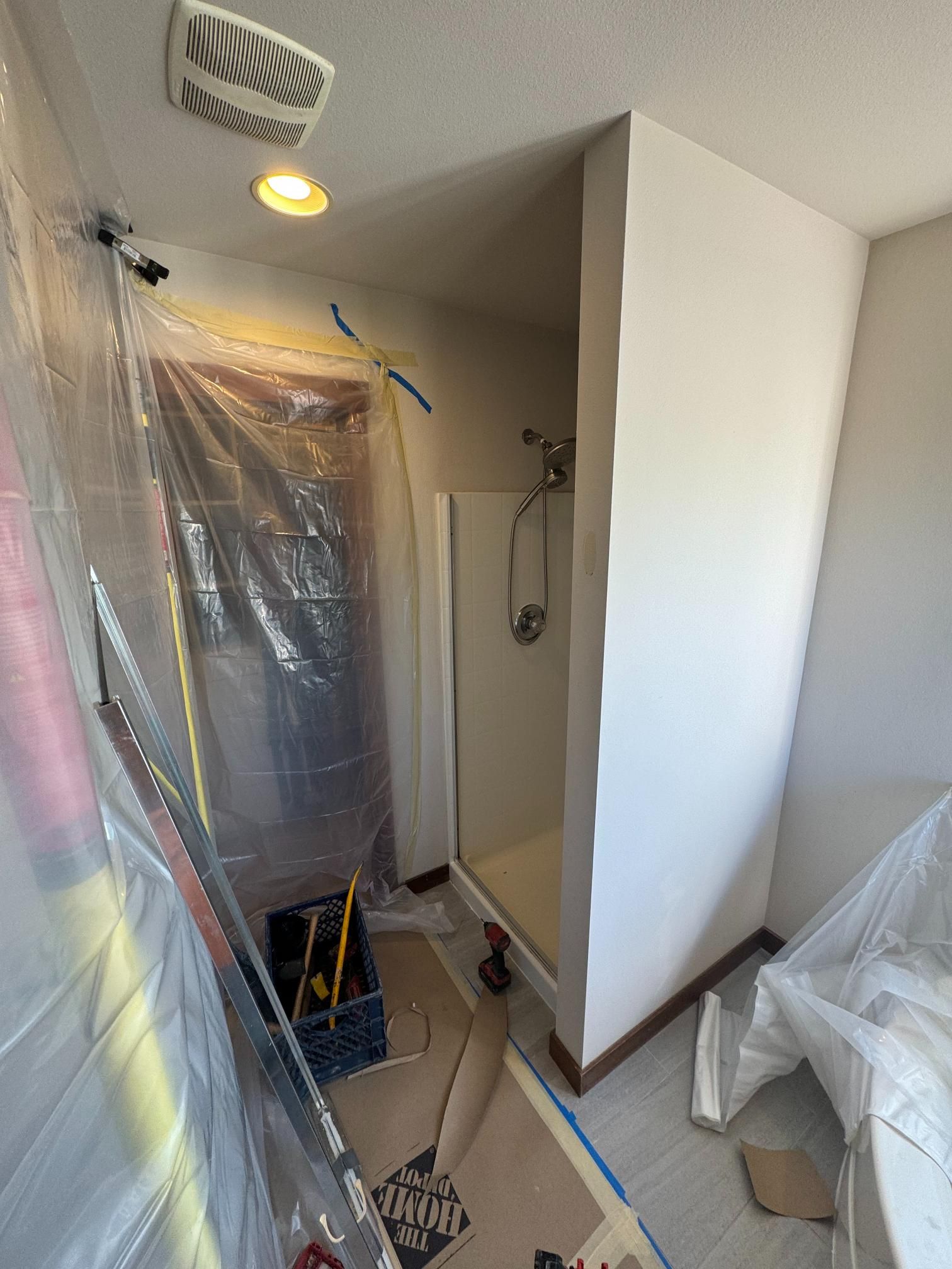 Bathroom undergoing renovation. Plastic sheeting protects fixtures. Shower stall, tools visible. Neutral paint and trim.