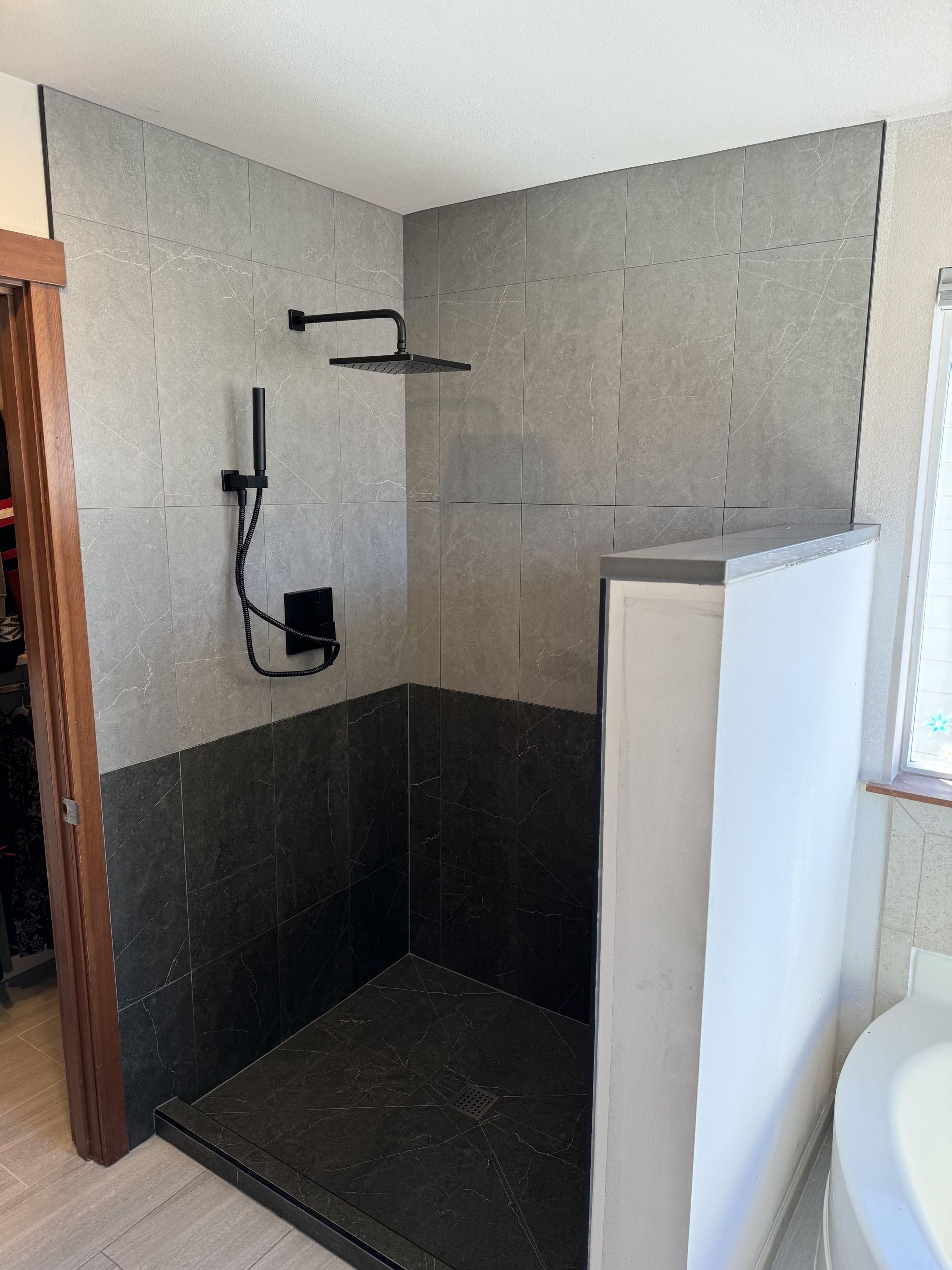 Gray and black tiled shower with black fixtures; showerhead and hand shower.