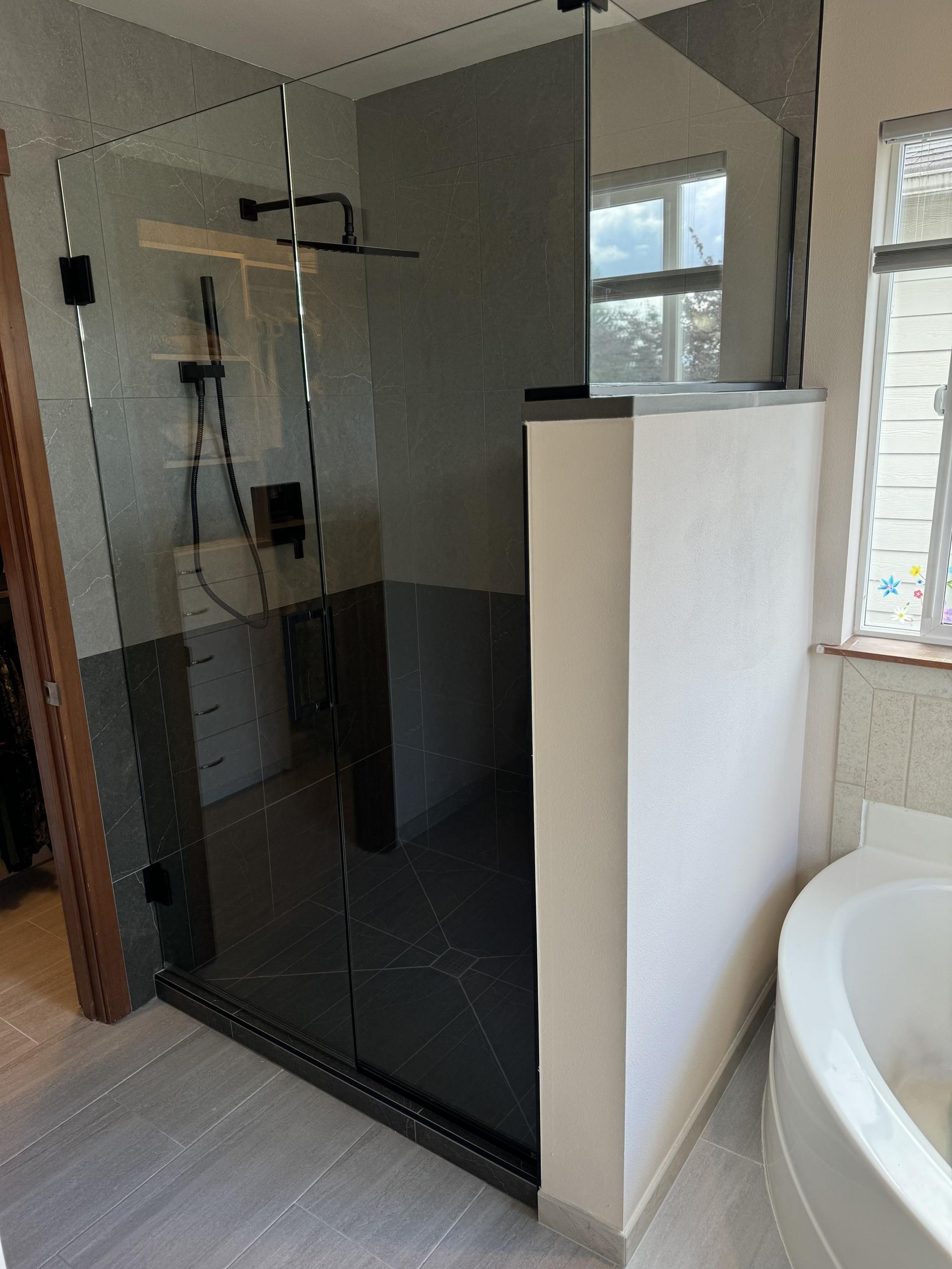 Modern bathroom with dark shower enclosure, white walls, and a partial view of a white tub.