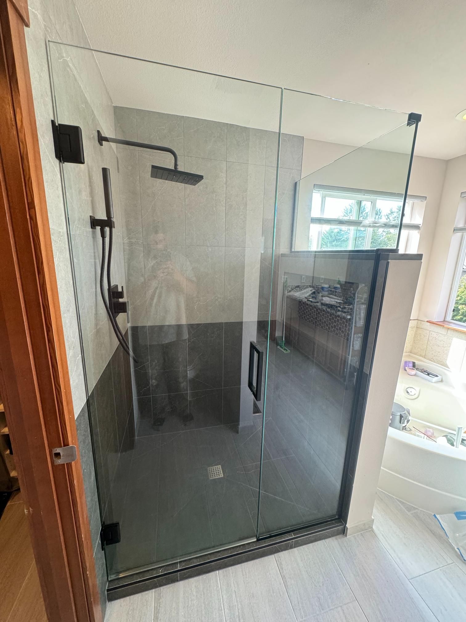 Modern walk-in shower with gray tiles, black fixtures, and glass enclosure.