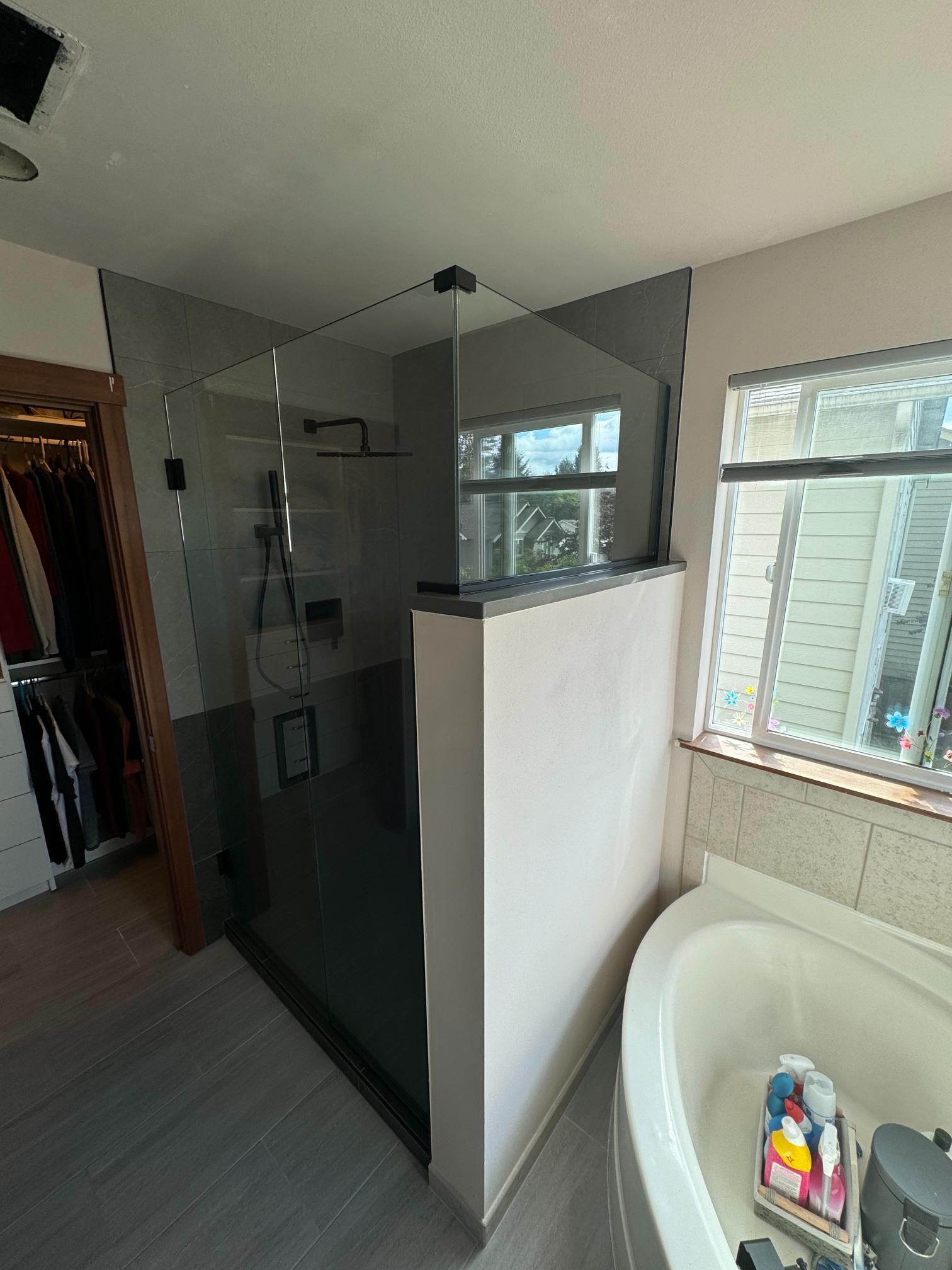 Modern bathroom with a glass shower, a tub, and a window.