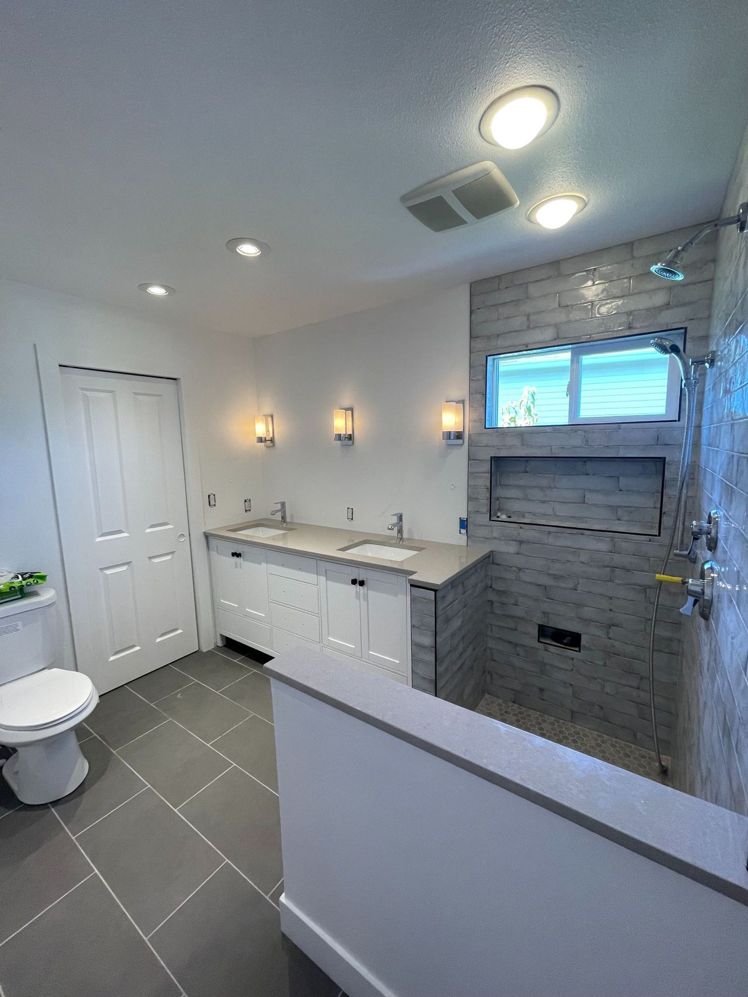 Modern bathroom with gray tiled floor, white vanity with double sinks, and walk-in shower.
