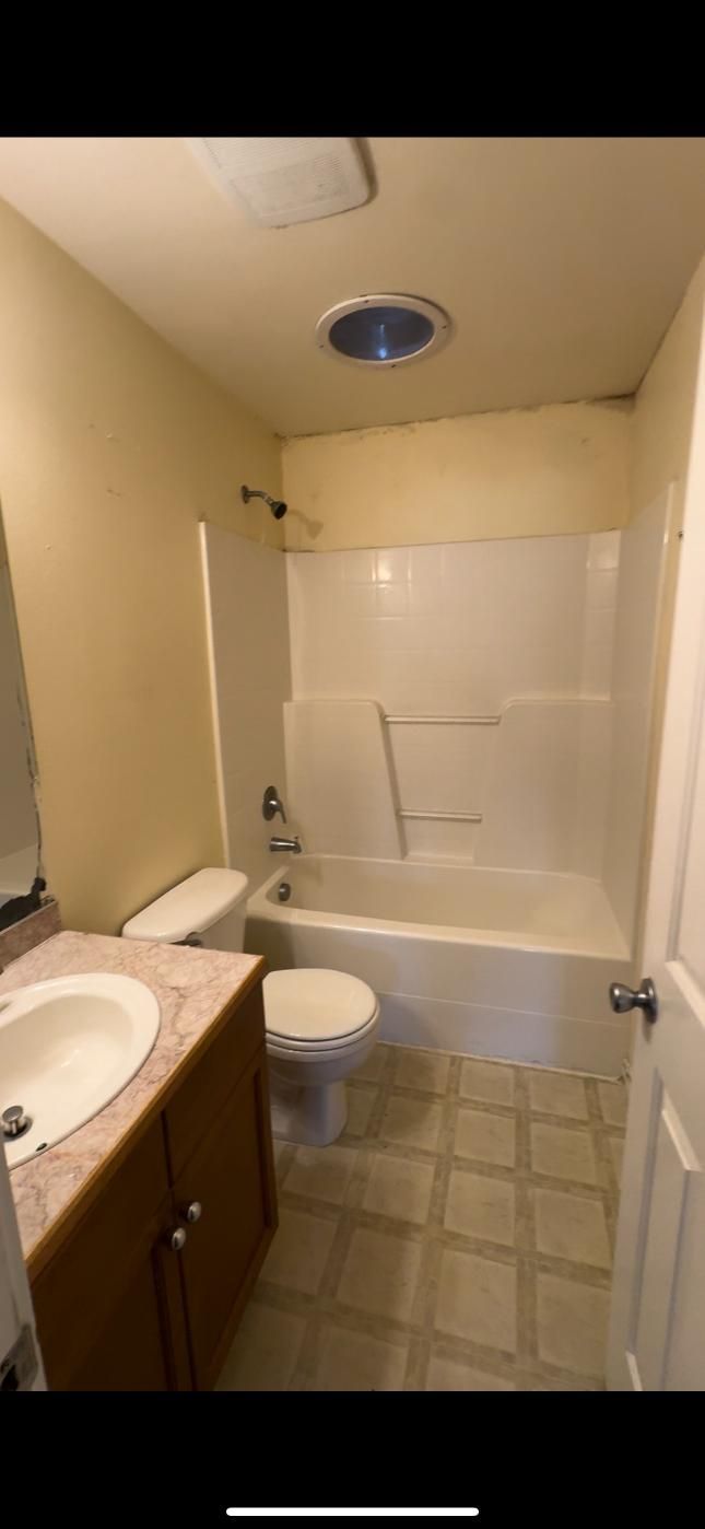 A small bathroom with a white tub, toilet, and sink, and tan walls.