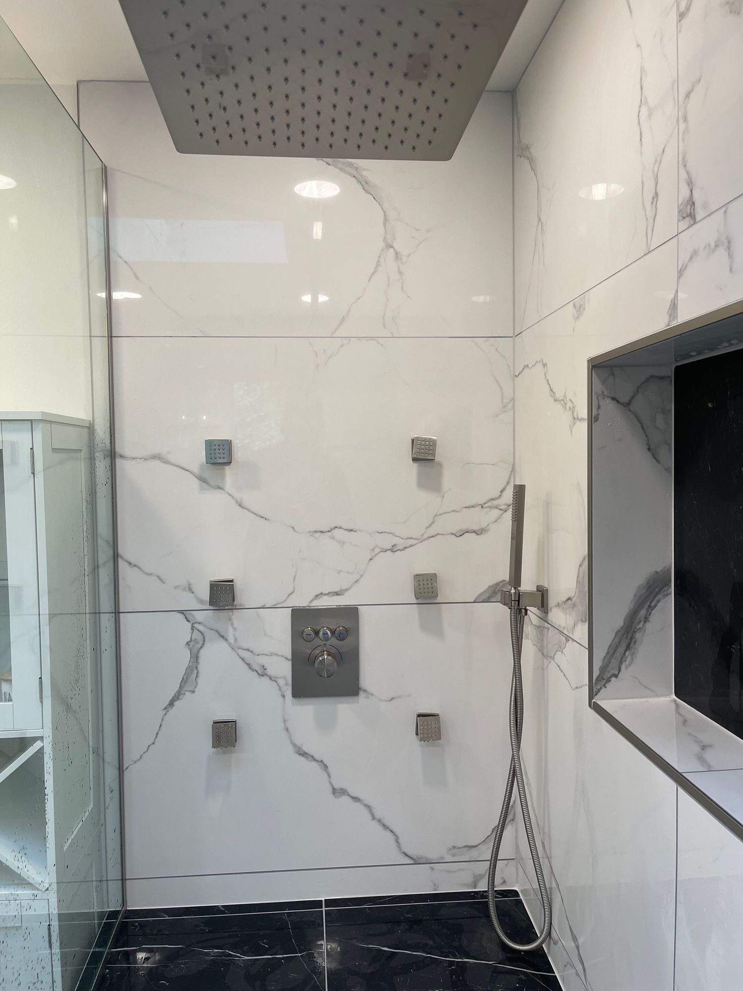 Modern shower with white marble-look tiles, a large square rain showerhead, and multiple body spray jets.
