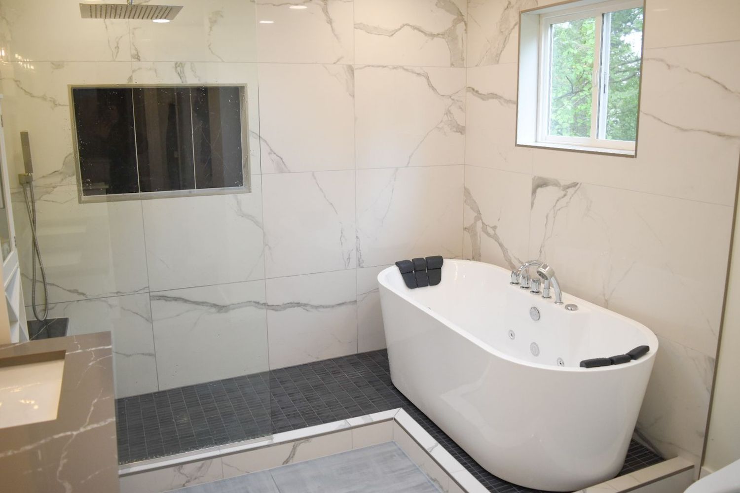Modern bathroom with white marble tile, freestanding tub, and a small window.