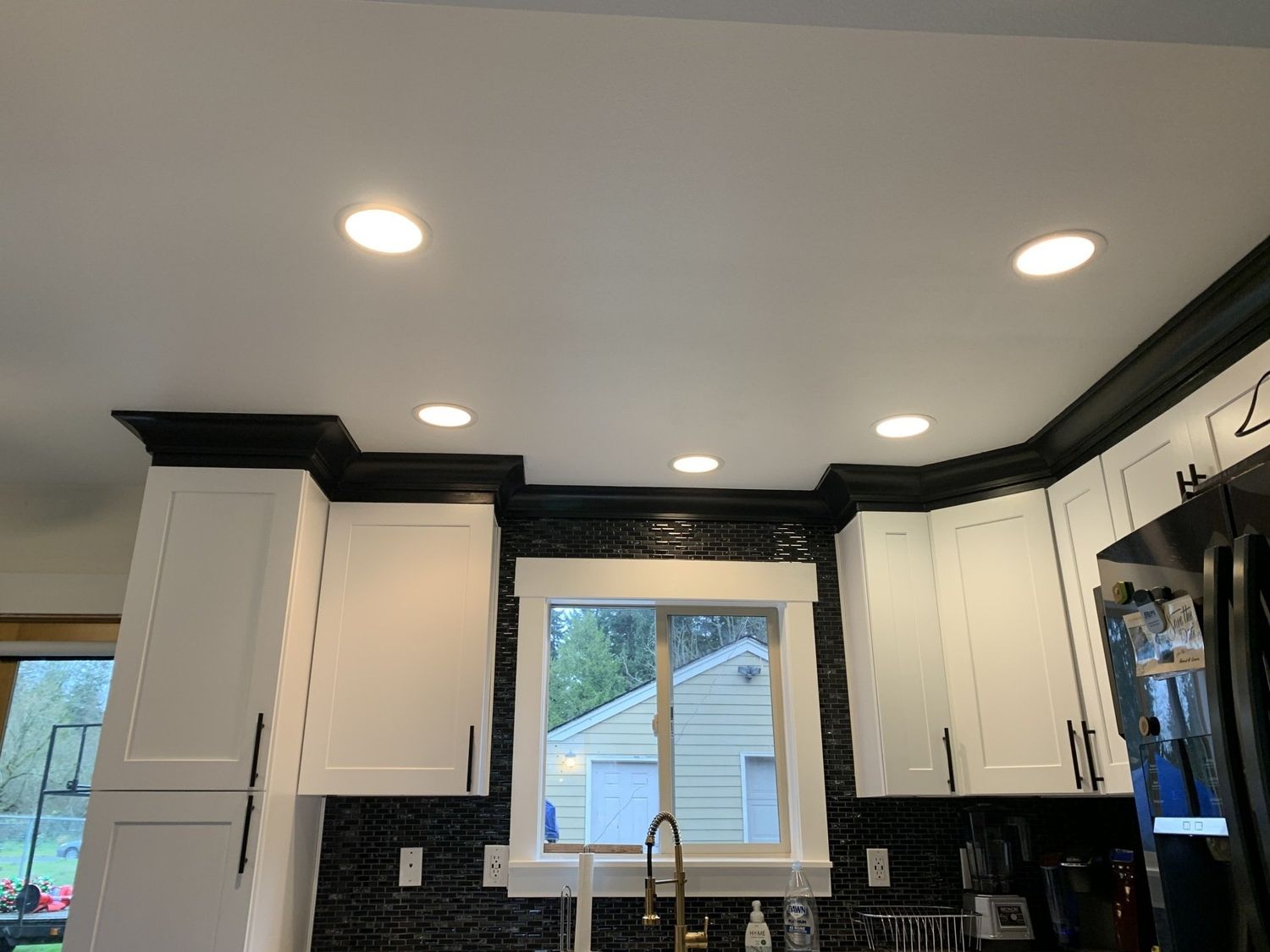 White kitchen cabinets with black trim and recessed lighting. Window with a view.