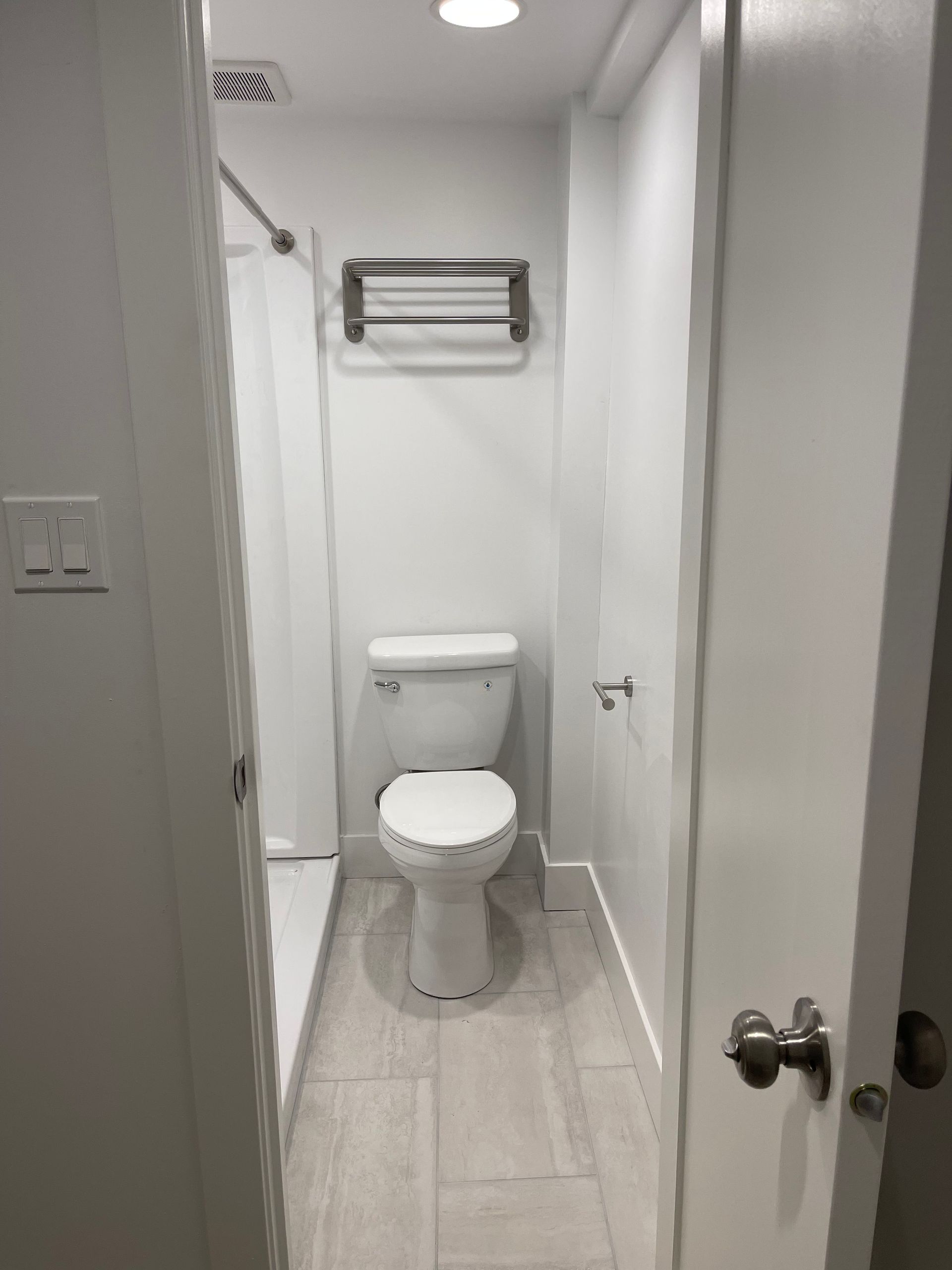 Small white bathroom with toilet, towel rack, and shower stall.