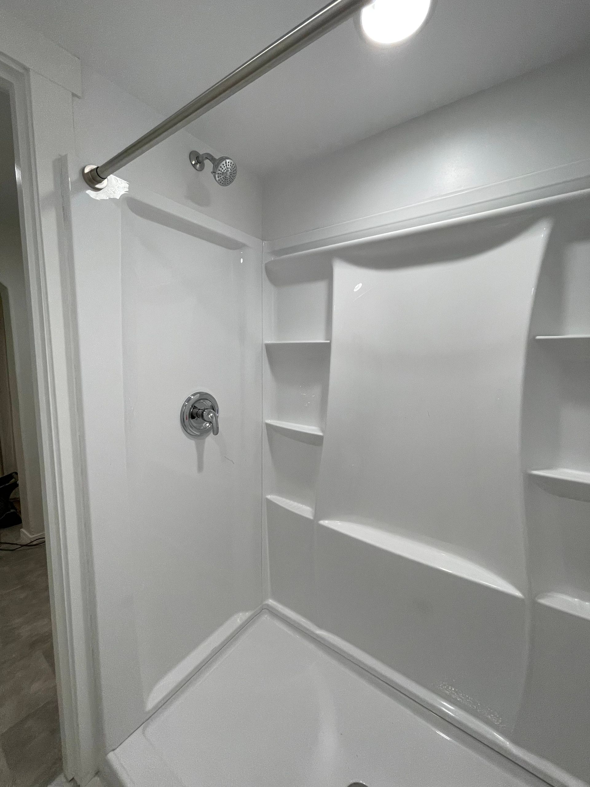 White shower stall with built-in shelves, chrome fixtures, and a shower rod.
