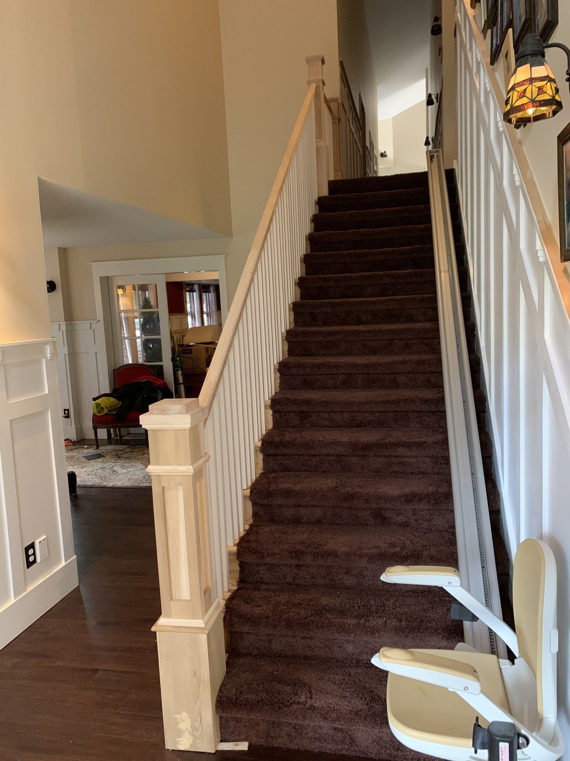 Staircase with brown carpet, white banister, and a beige stair lift.  View of the stairs from the bottom.