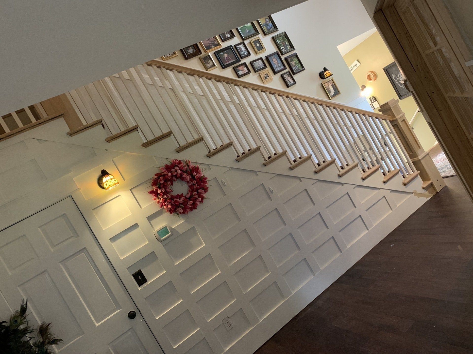Staircase with white railing and paneling, decorated with a wreath and photos on the wall.