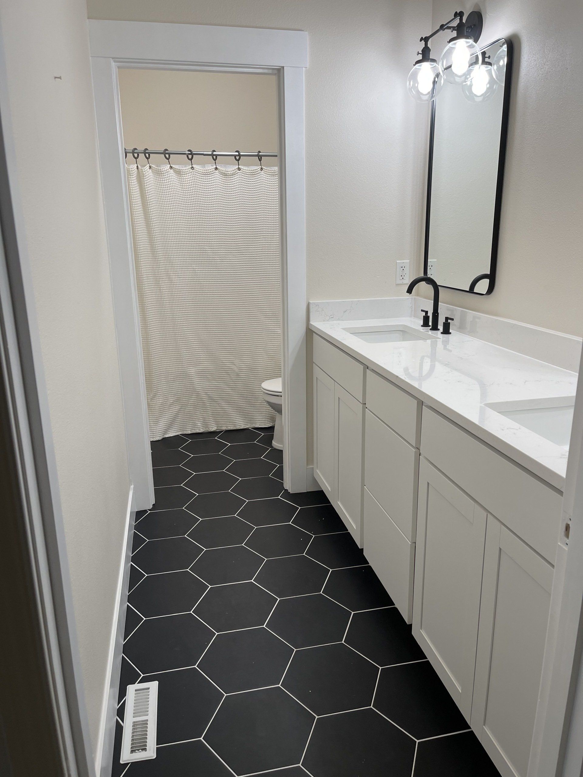 Bathroom with black hexagon tile floor, white cabinets, and a long mirror with three lights.