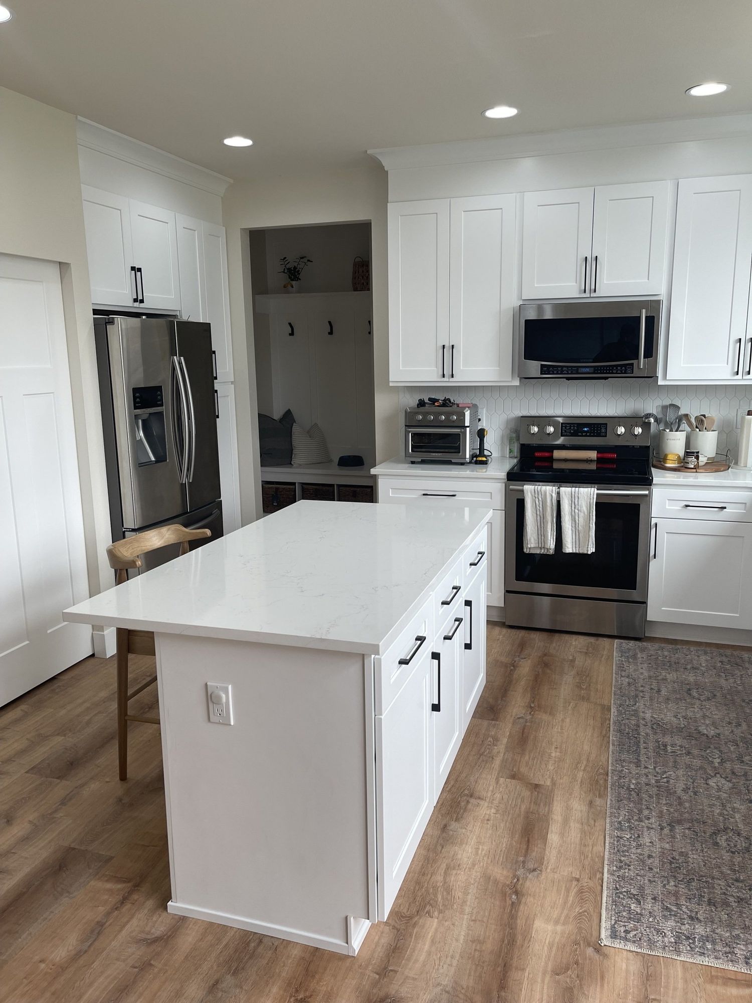 White kitchen with island, stainless steel appliances, and wooden flooring.