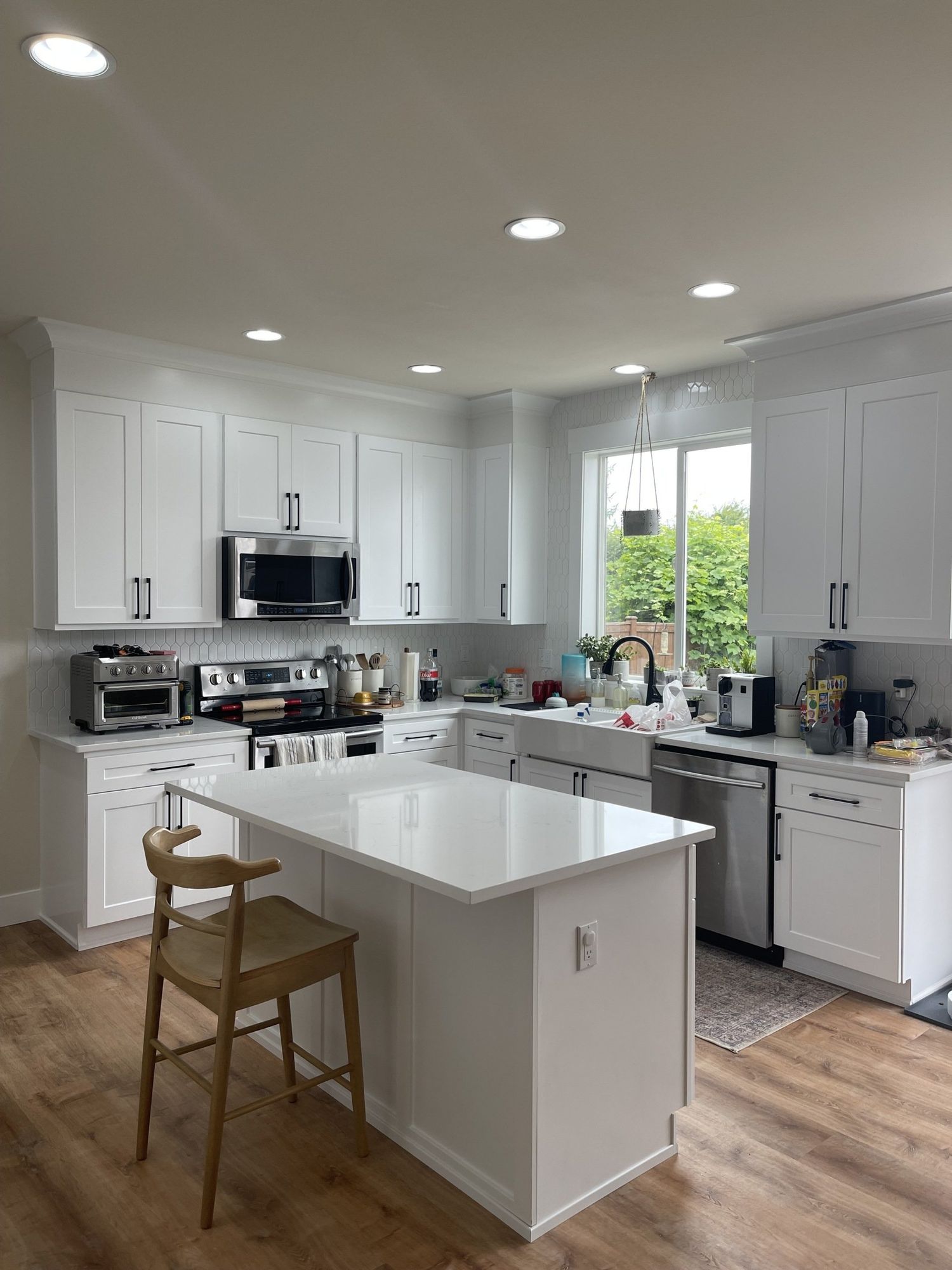 White kitchen with island, cabinets, appliances, and wood floor. Sunlight streams in.