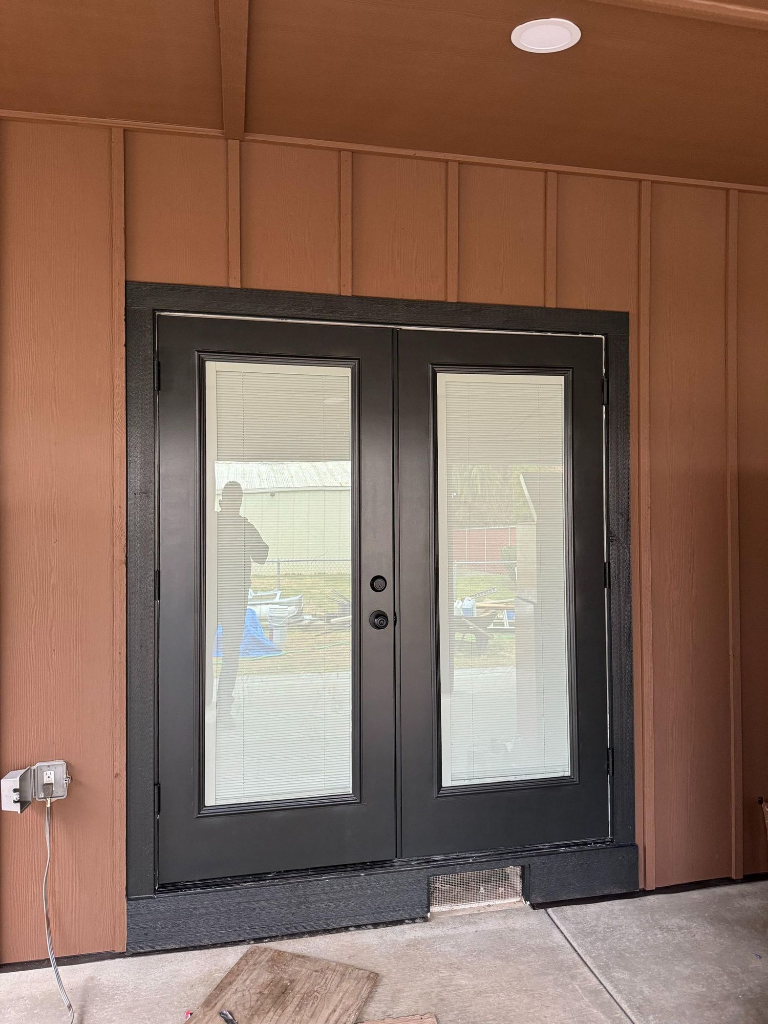 Black double doors with glass panels and blinds, set in a brown exterior wall.