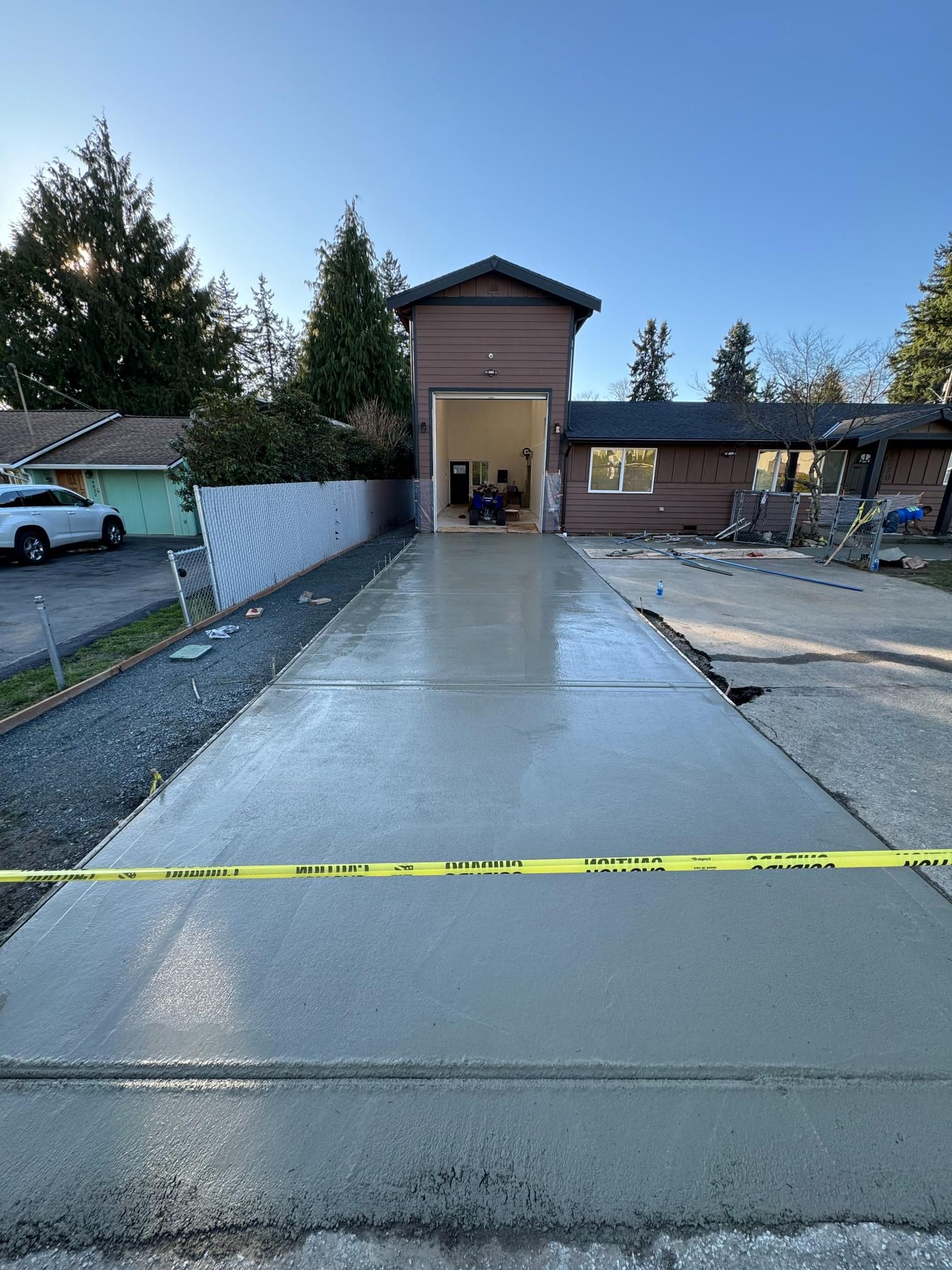 Freshly poured concrete driveway in front of a house. Yellow caution tape in foreground.