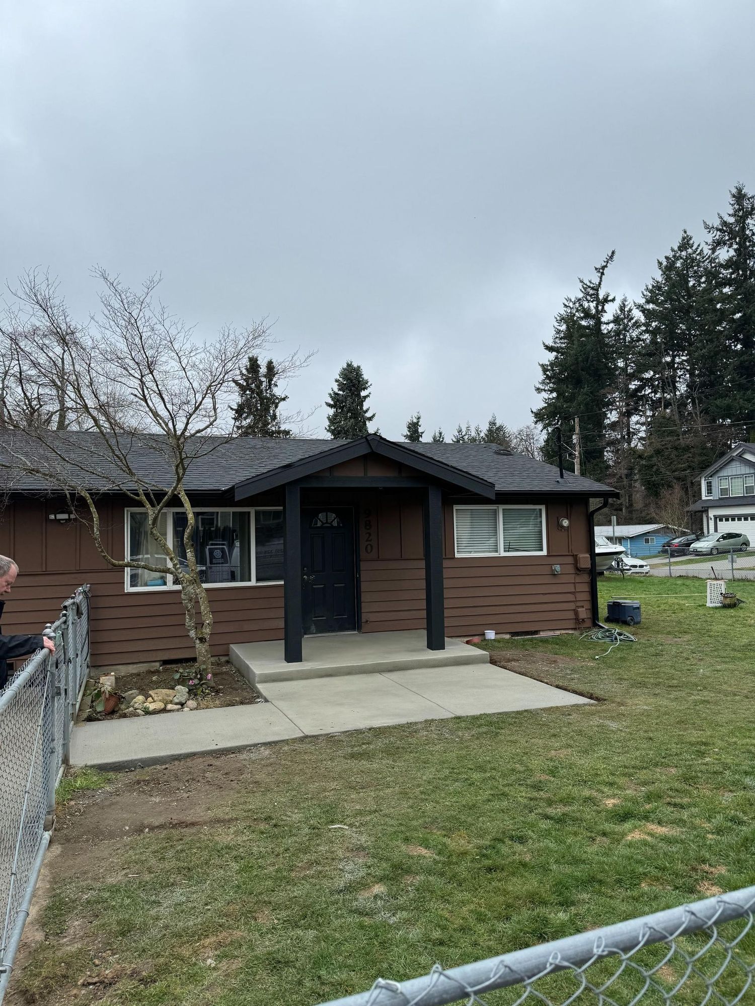 Brown house with black trim, porch, and a chain link fence in front. Overcast day.