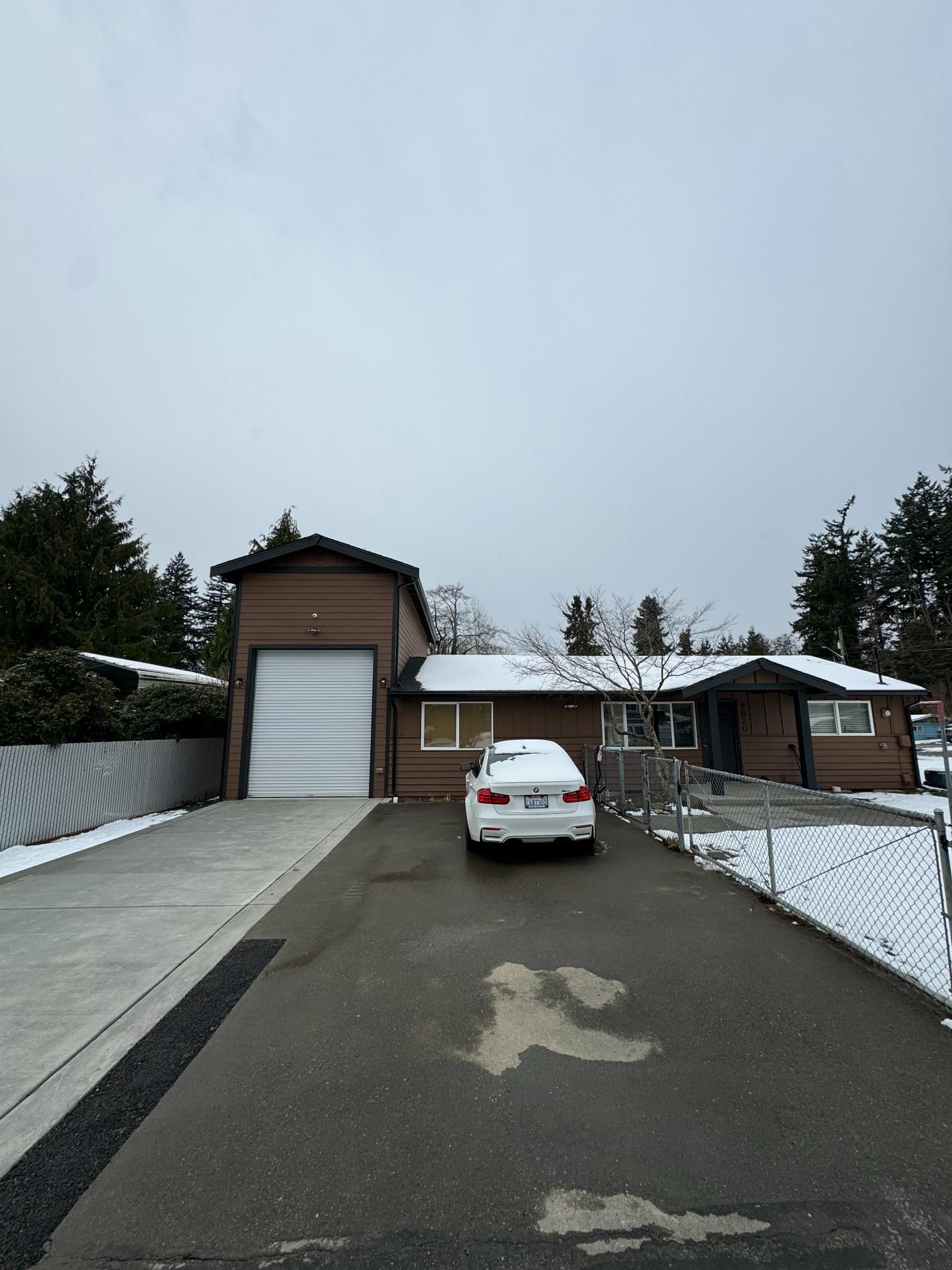 Brown house with attached garage, snow-covered roof and ground, a car parked in driveway under overcast sky.