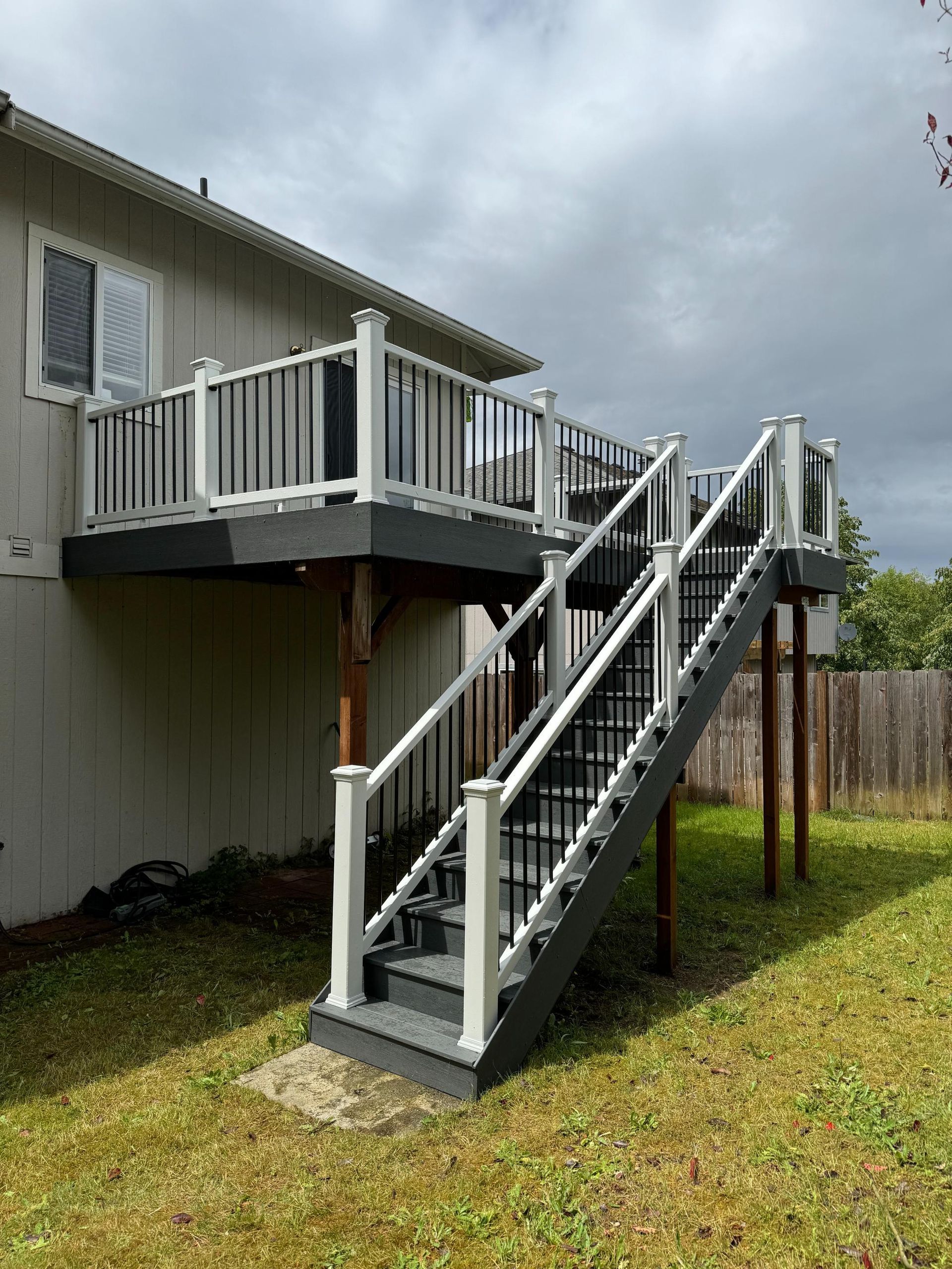 Gray deck with white railing and stairs against a beige house, cloudy sky.