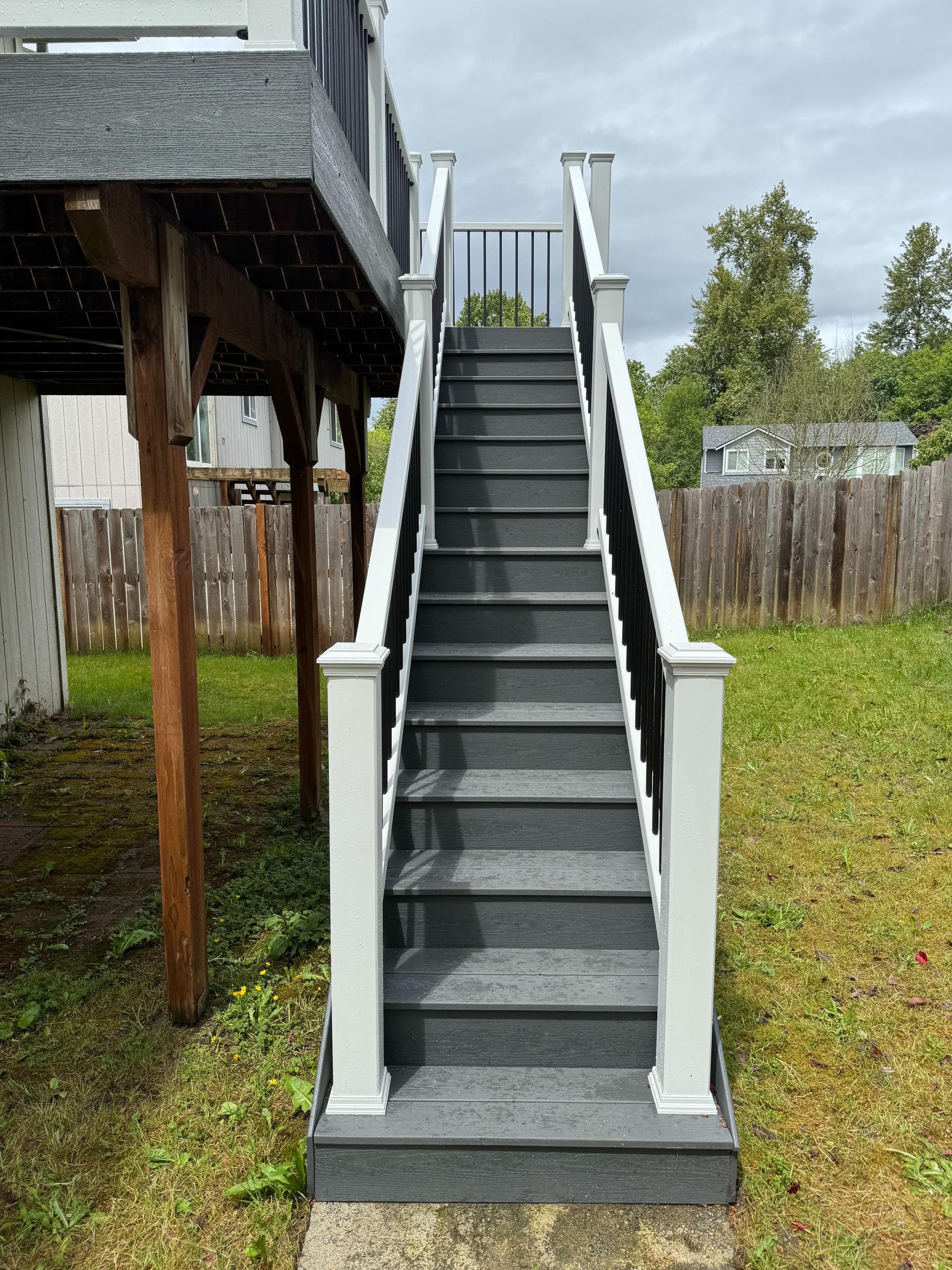 Outdoor staircase leading up to a deck, gray steps with white and gray railing, green lawn.