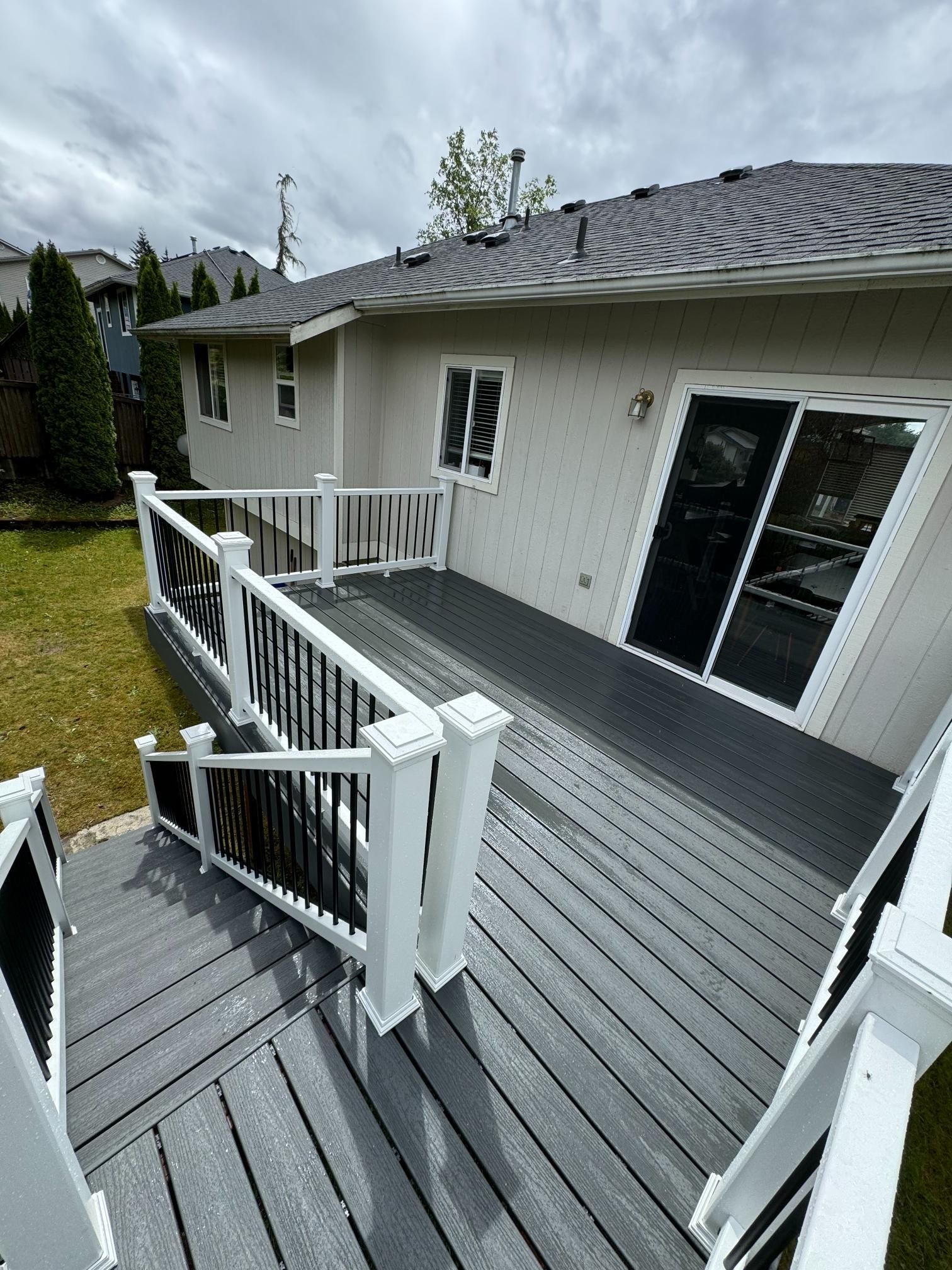 Gray deck with black railing, white posts, and a house with a gray roof and siding.