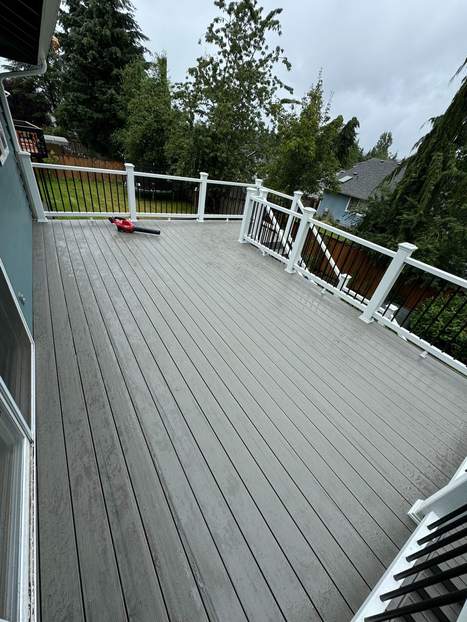 Gray composite deck with white railings, looking out to green trees and overcast sky.