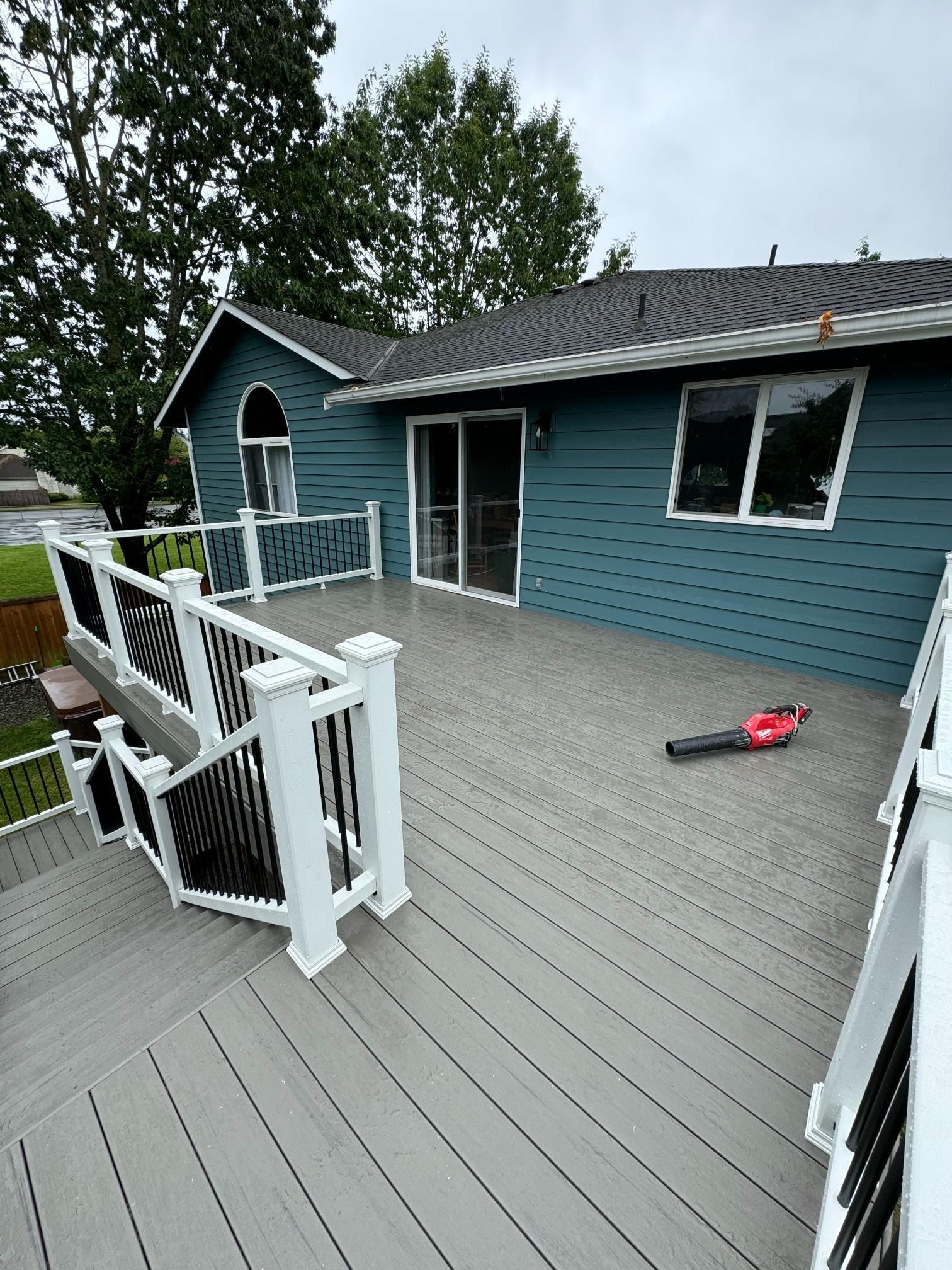 Gray deck with black railing and blue house. A leaf blower is on the deck.