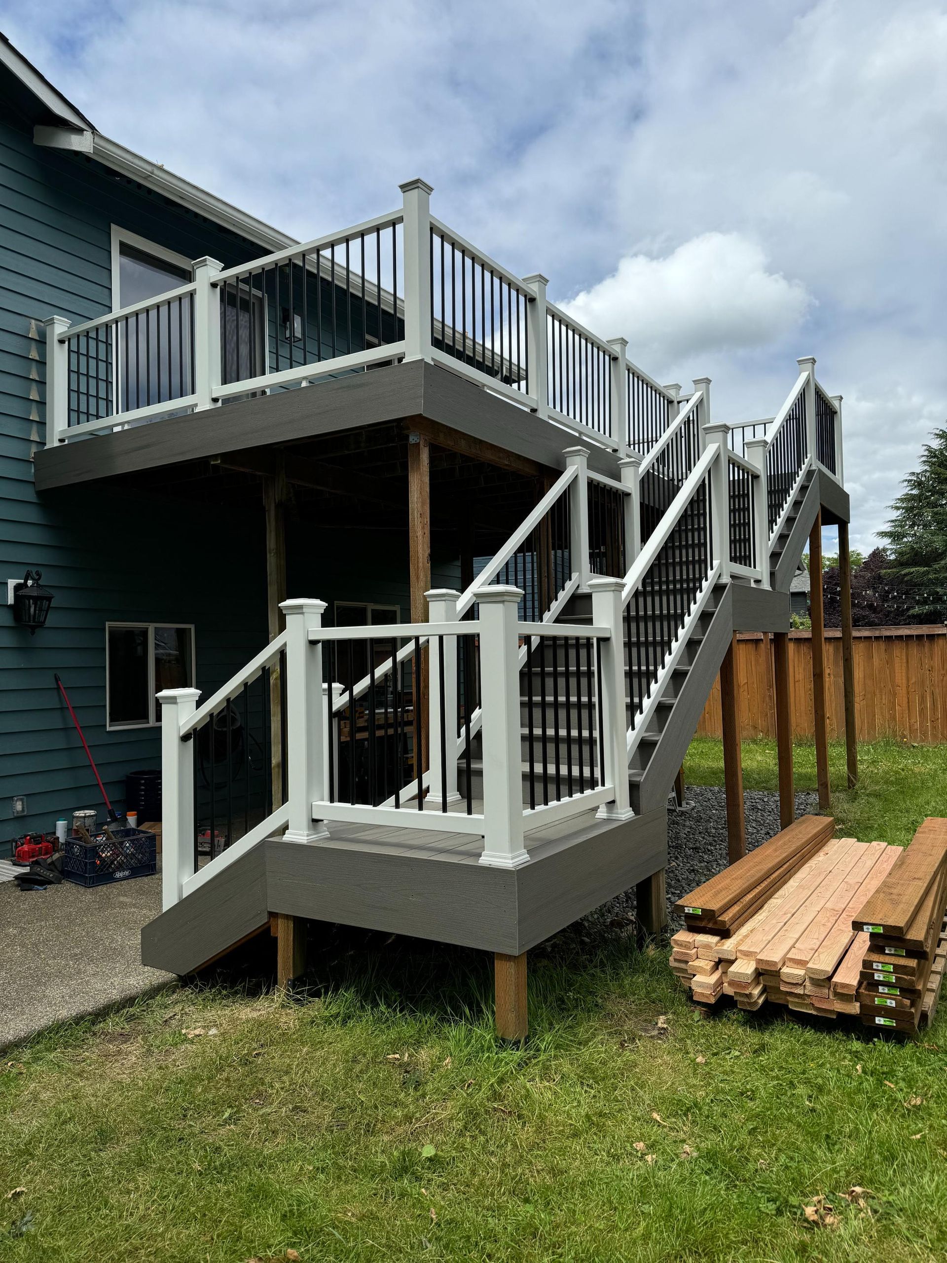 Multi-level deck attached to a teal house, white railing, black balusters, and stairs on green lawn.