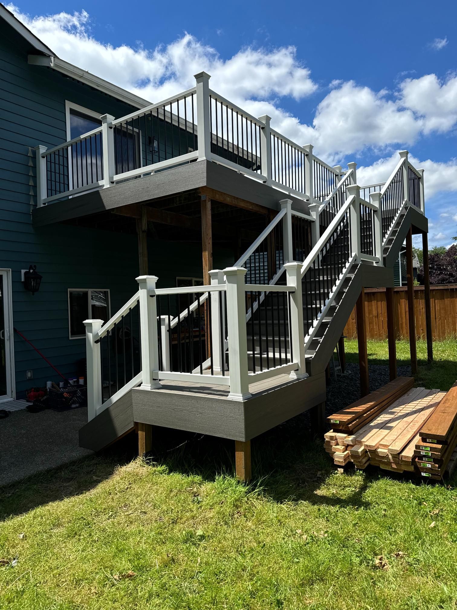 Two-tiered deck with white railings and black balusters attached to a dark blue house. Stairs lead to each level.