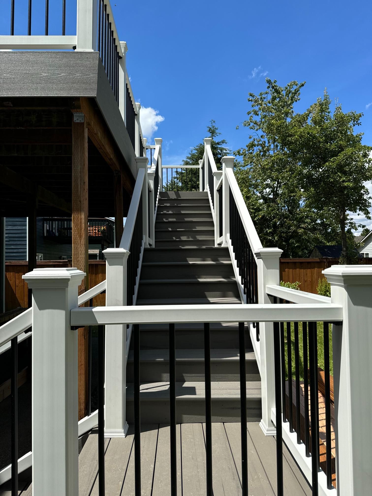 Outdoor staircase with gray steps and white and black railings, leading up to a deck.