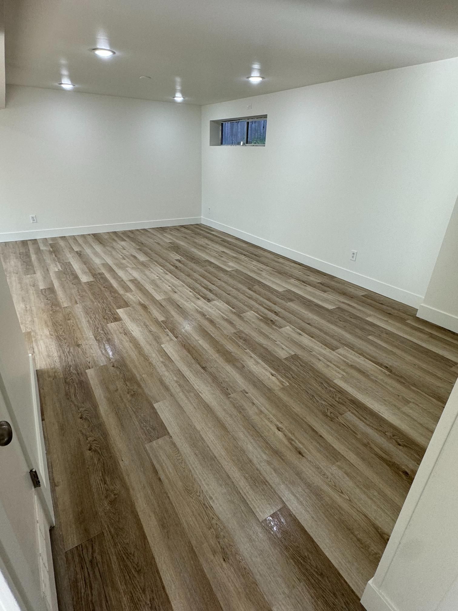 Empty room with wood-look flooring and white walls. Includes recessed lights and a small window.