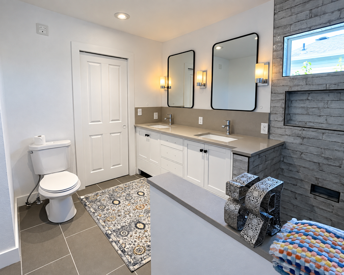 Bright modern bathroom with double vanity, toilet, patterned rug, and tiled shower wall.
